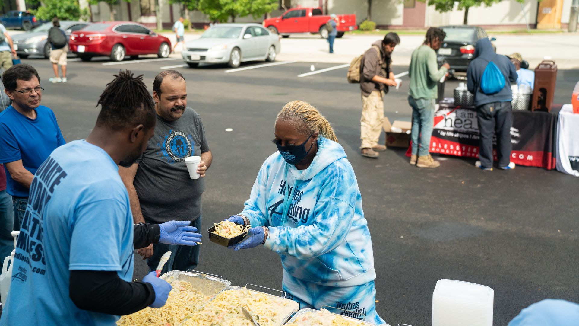 A woman is serving food to a group of people in a parking lot.