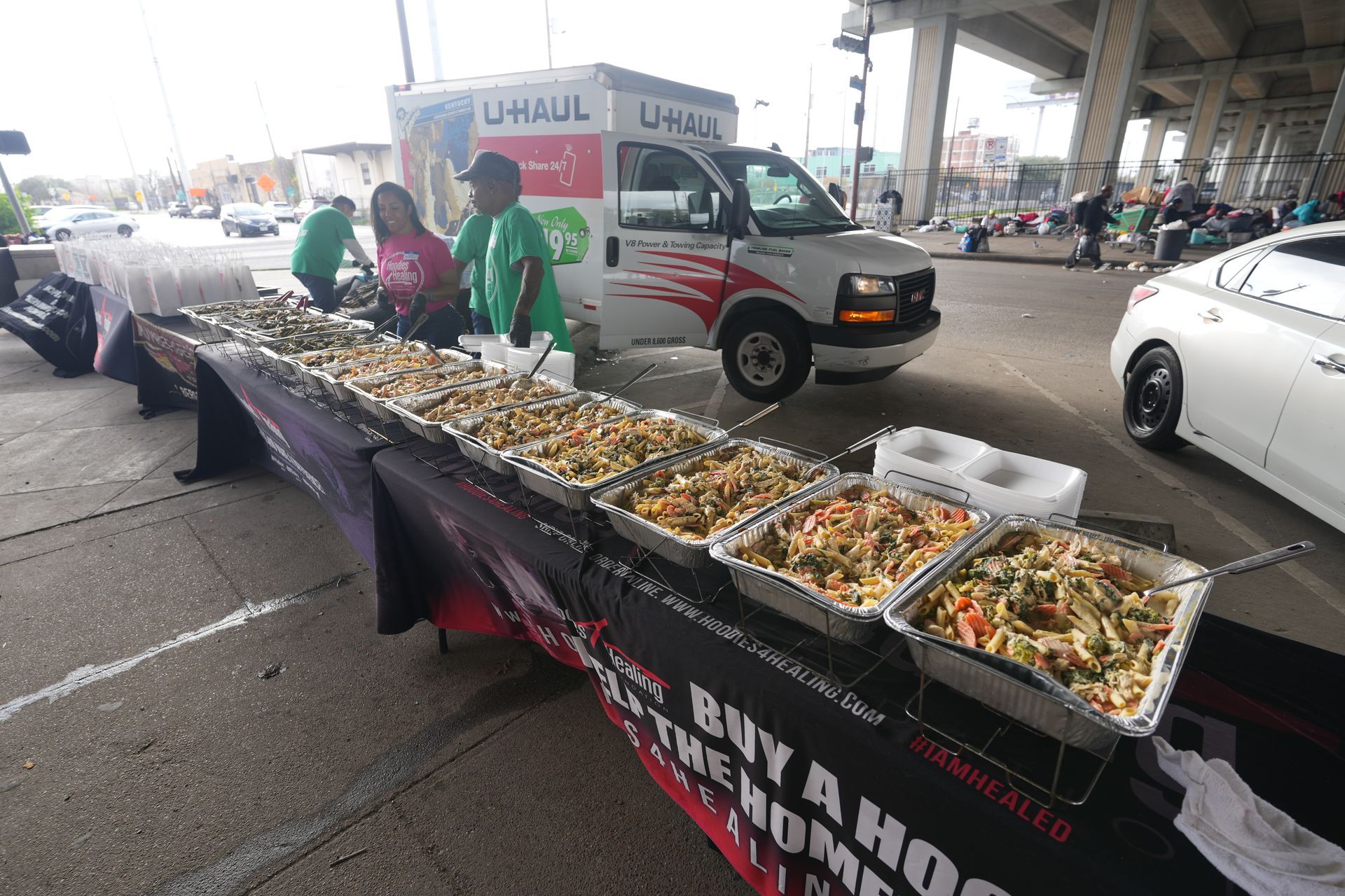 A uhaul van is parked in a parking lot next to a table filled with trays of food.