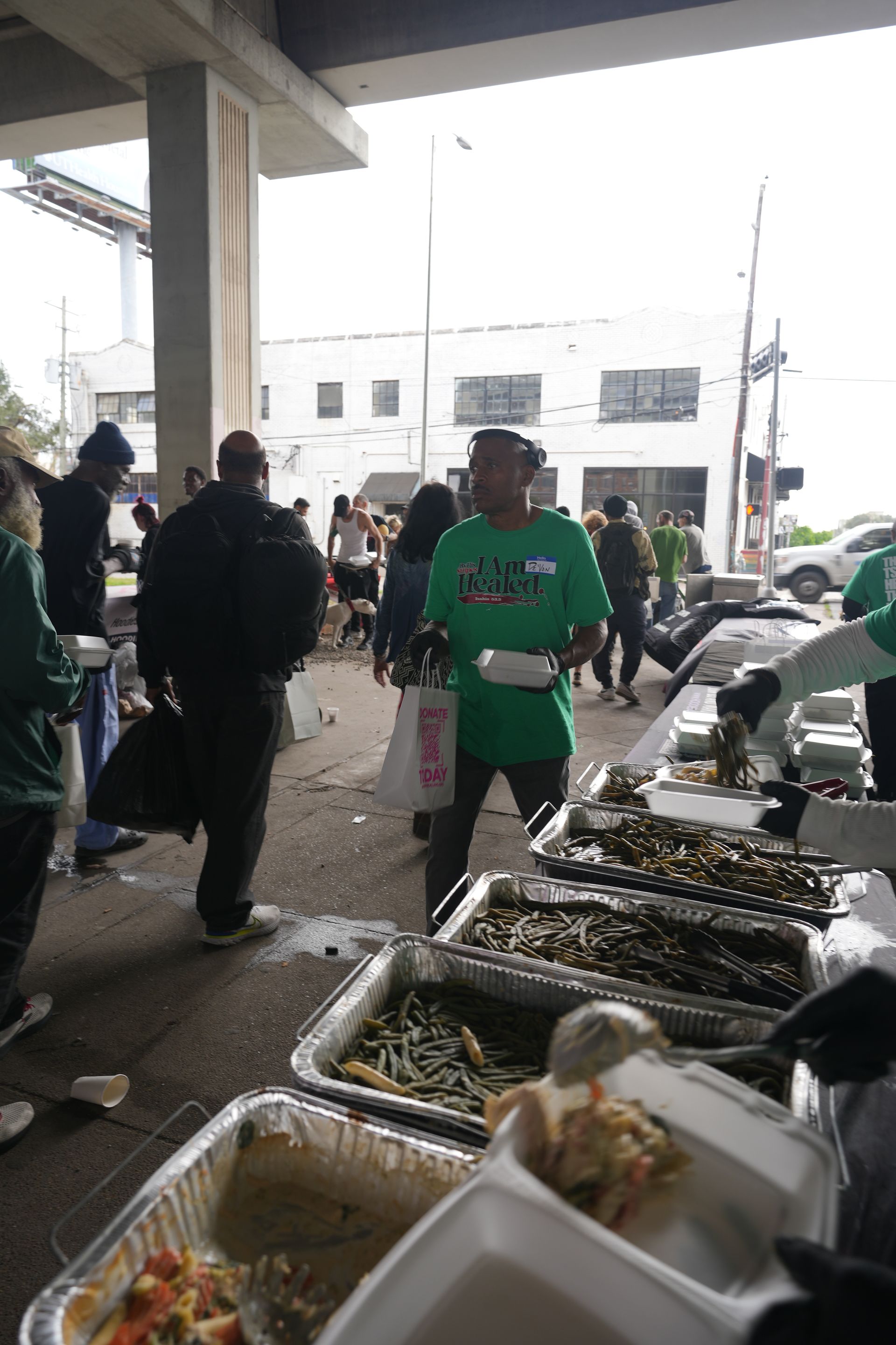 A man in a green shirt is standing in front of a table full of food.