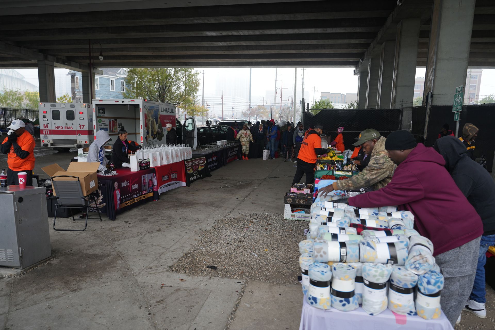 A group of people are standing around tables under a bridge.