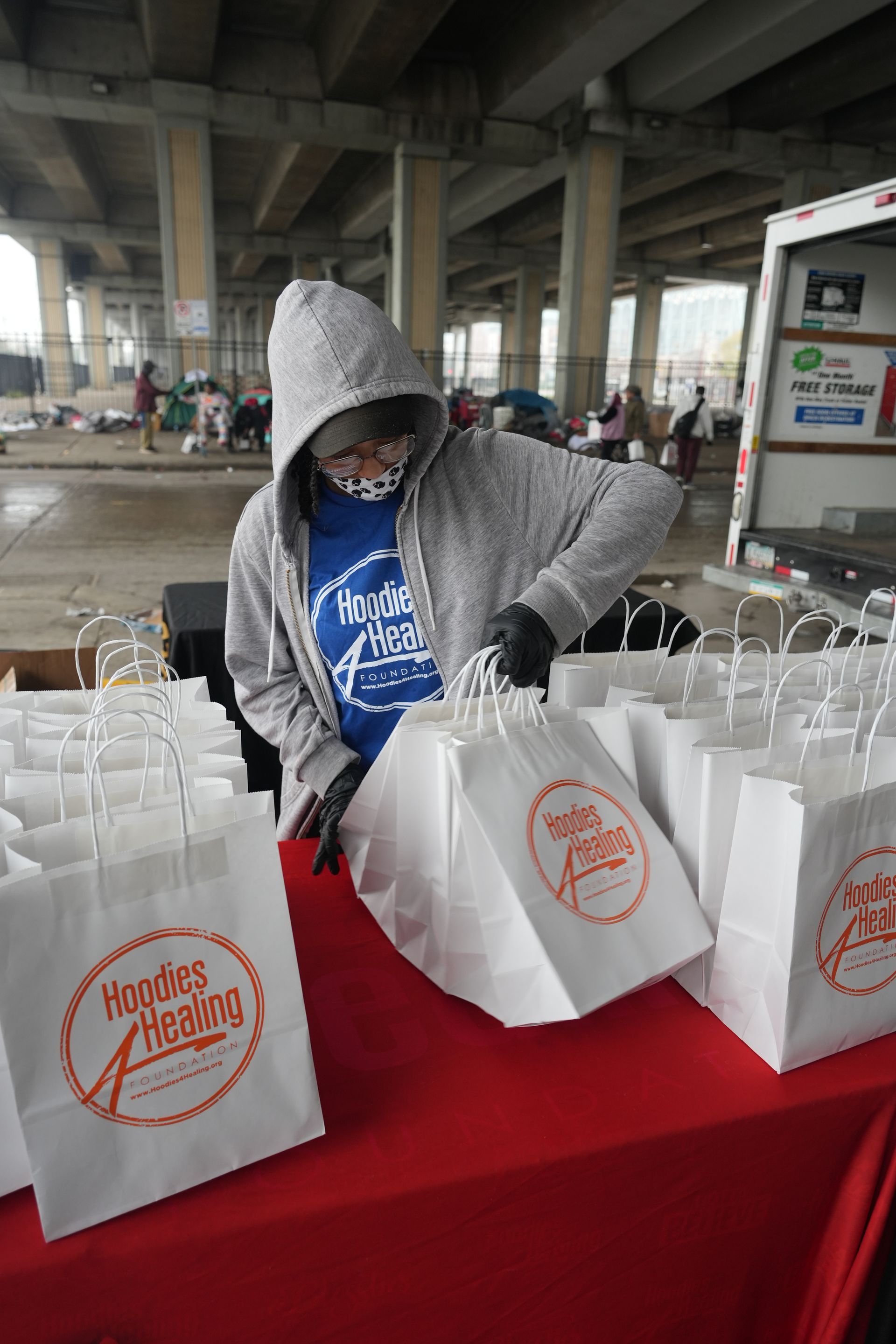 A man in a hoodie is standing at a table filled with paper bags.