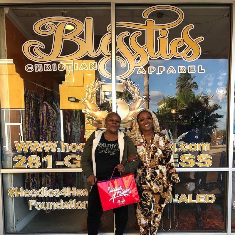 Two women are standing in front of a store called blissties christian apparel