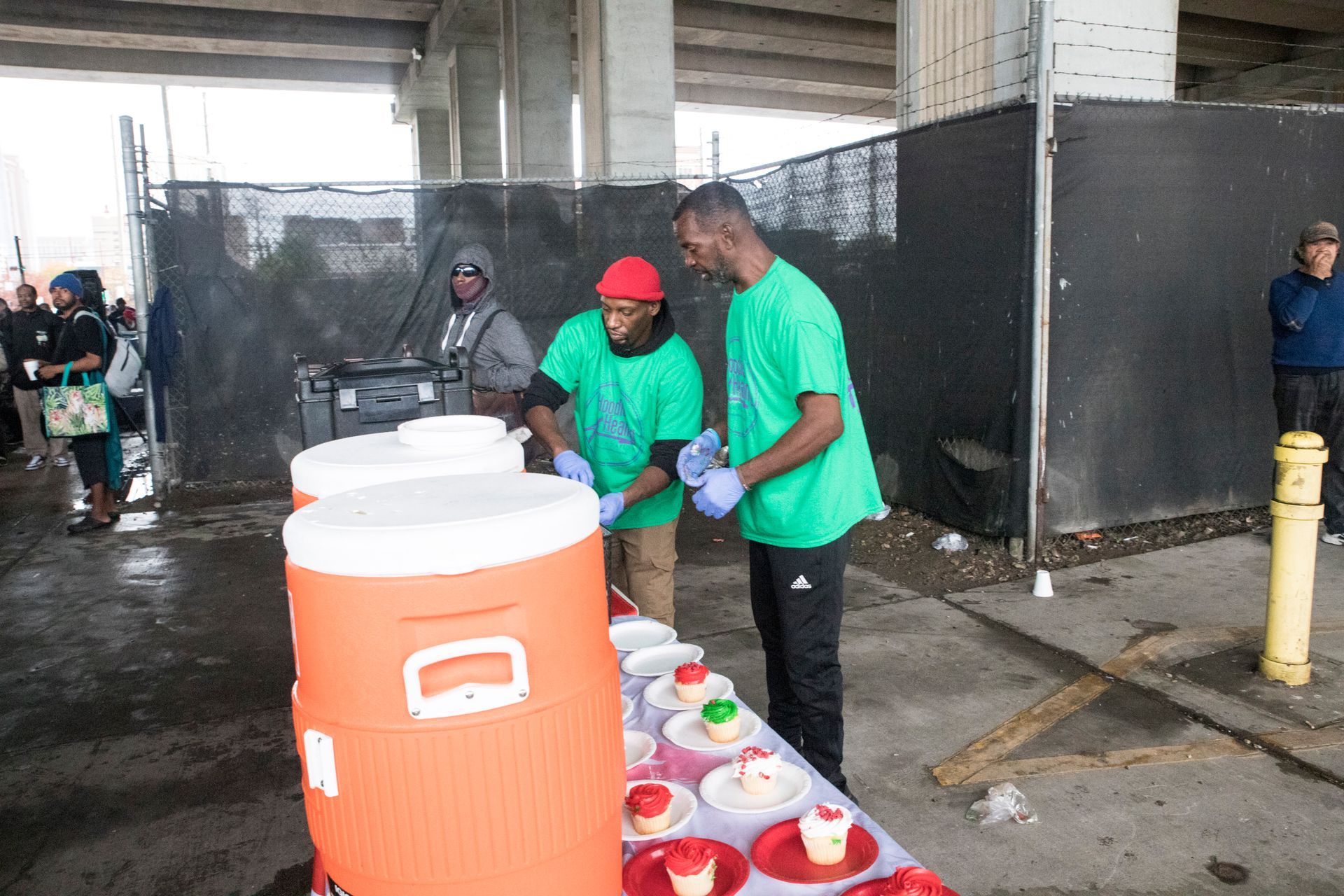 Two men in green shirts are standing at a table with orange jugs.