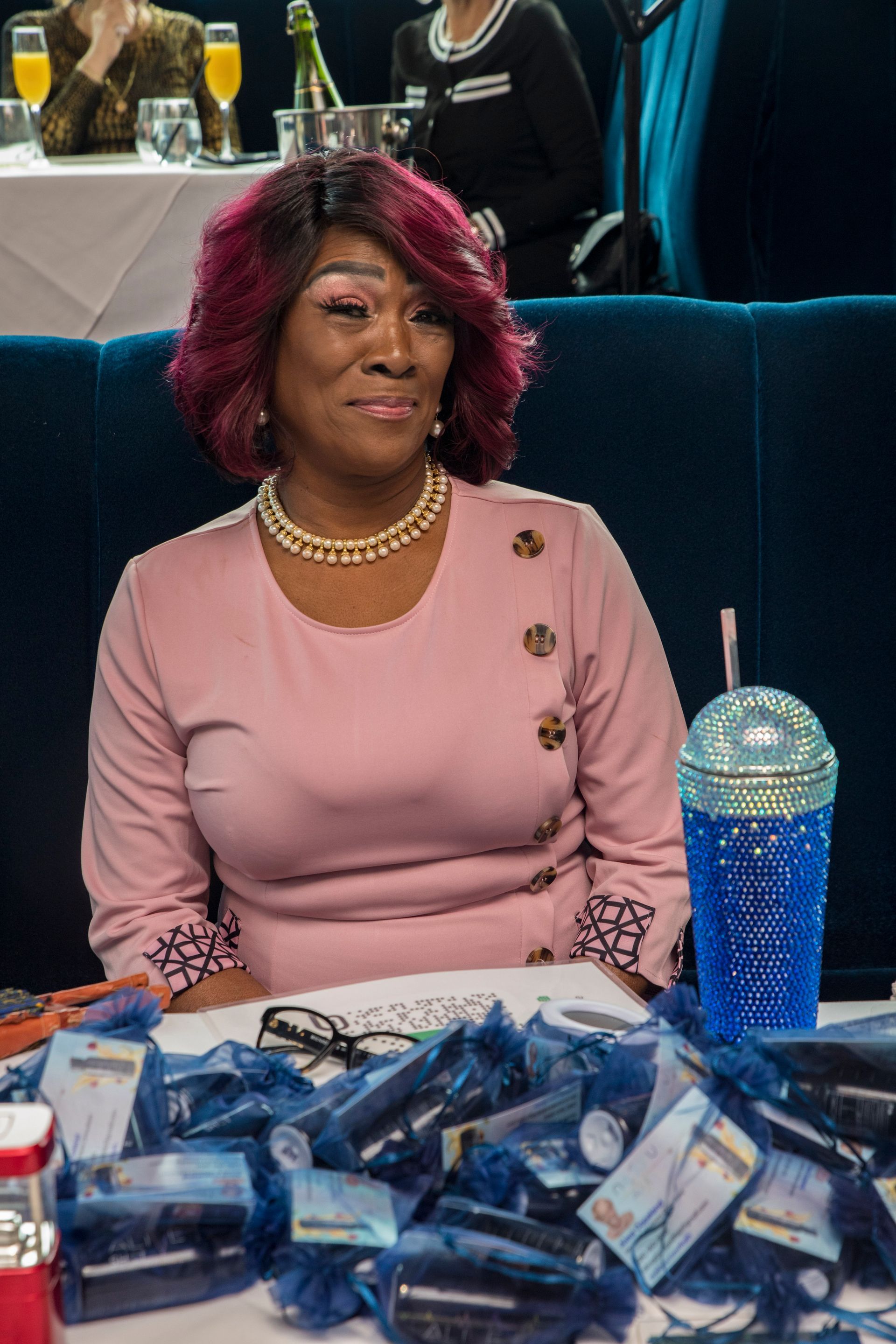A woman in a pink dress is sitting at a table with a cup of water.