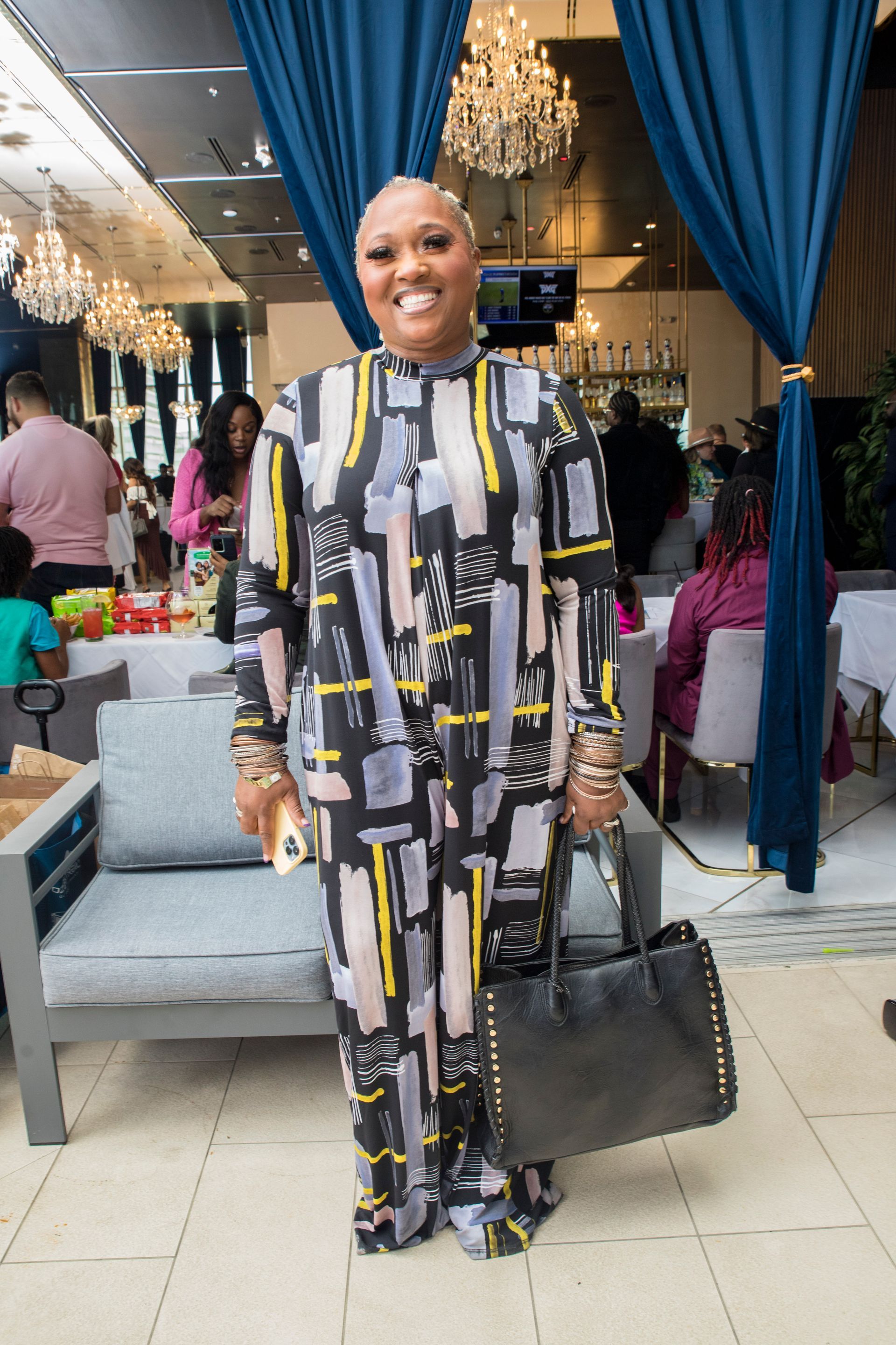 A woman in a jumpsuit is standing in a room holding a black purse.