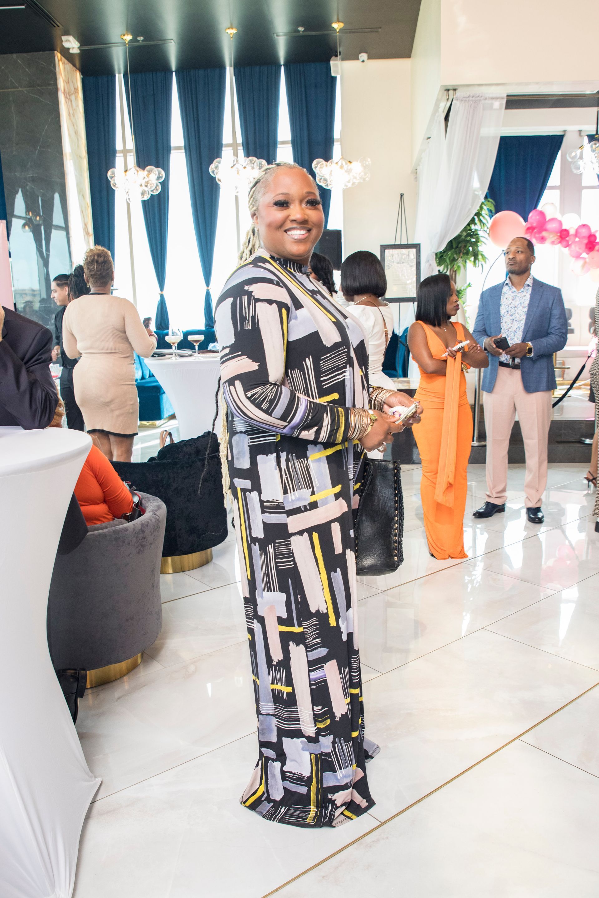 A woman in a dress is standing in a room with other people.