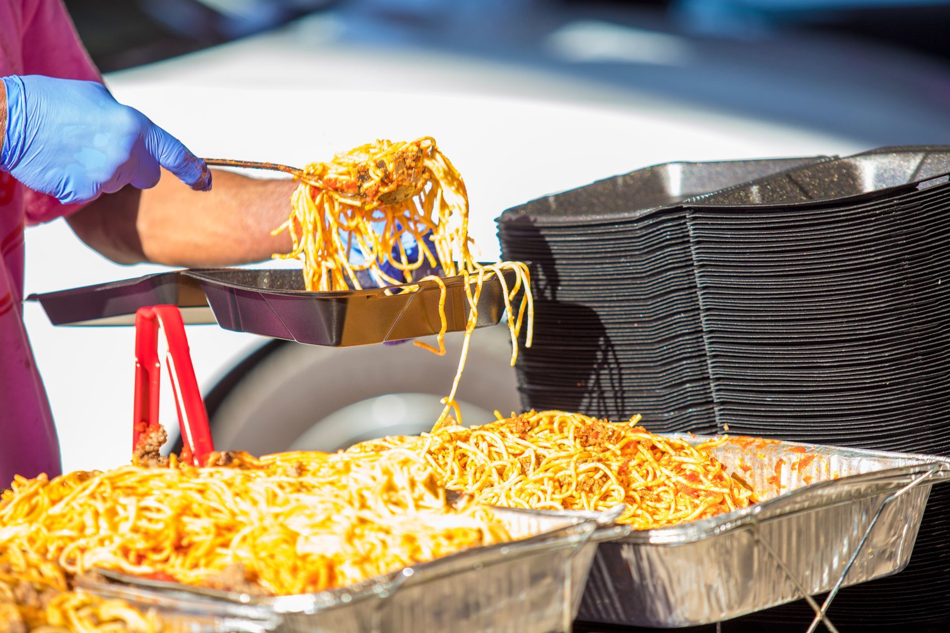 A person is serving noodles from a tray with tongs.