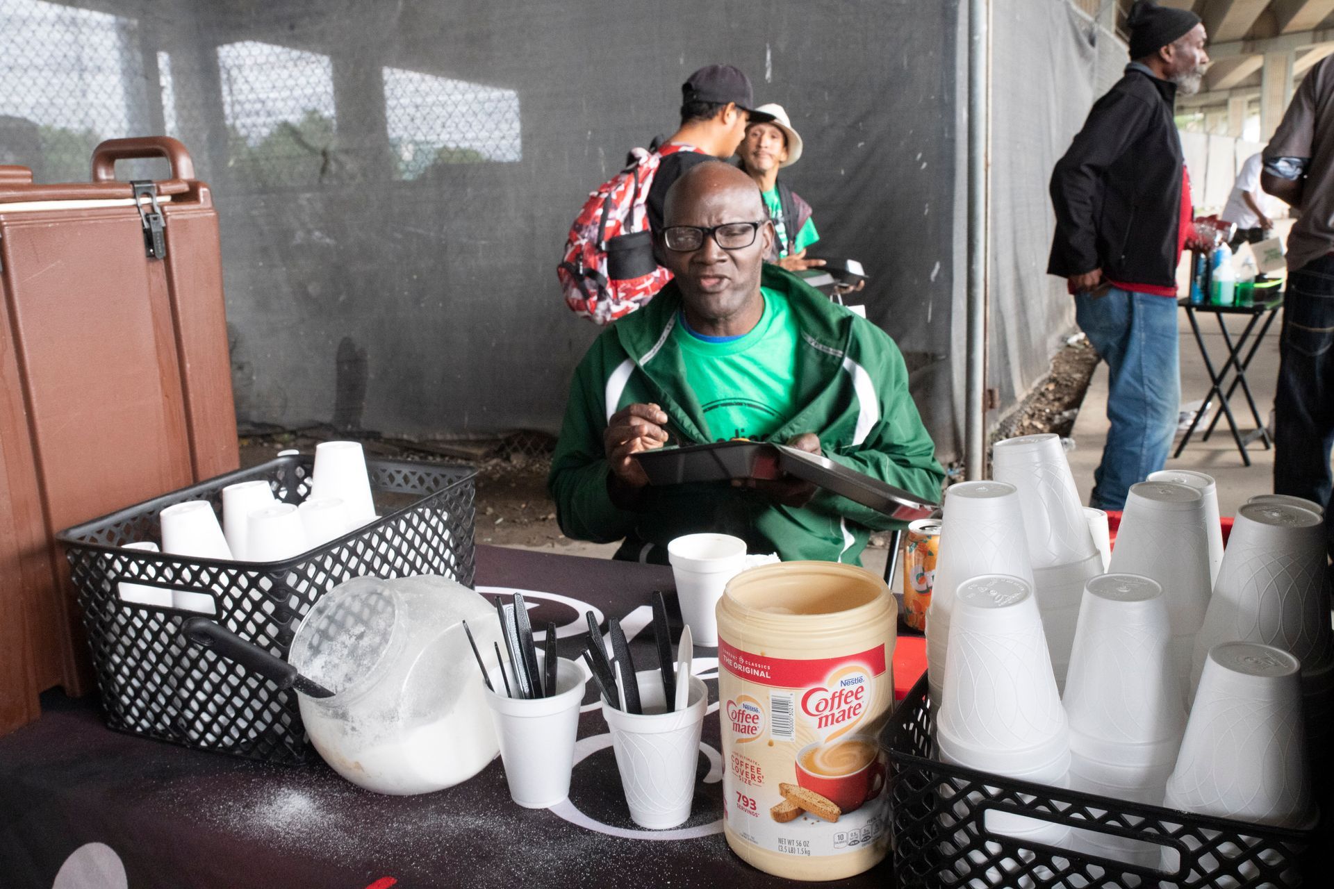 A man is sitting at a table with cups and a jar of peanut butter
