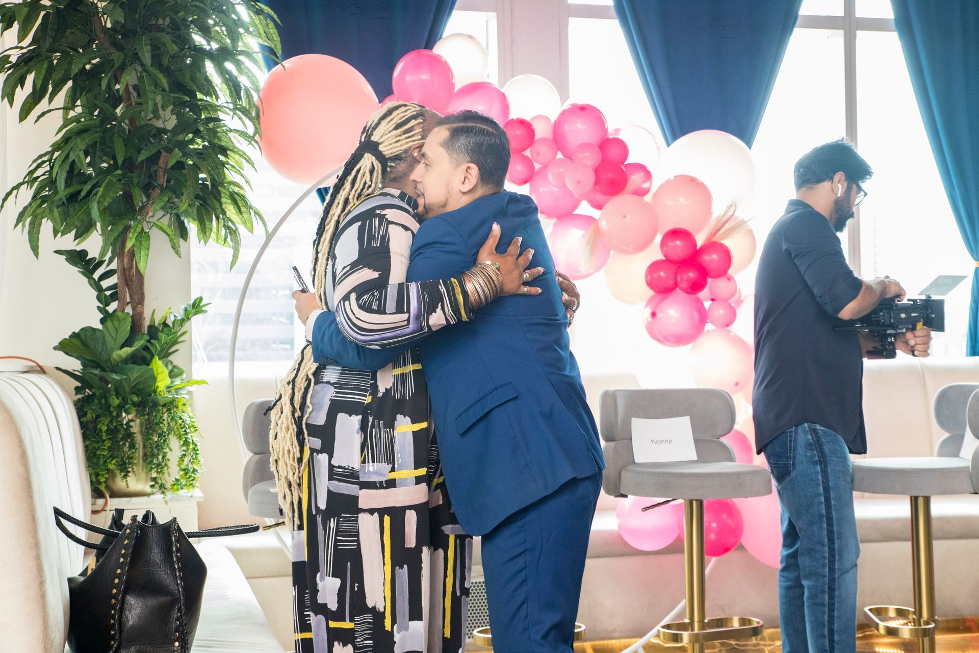 A man in a suit is hugging a woman in a room with pink balloons.