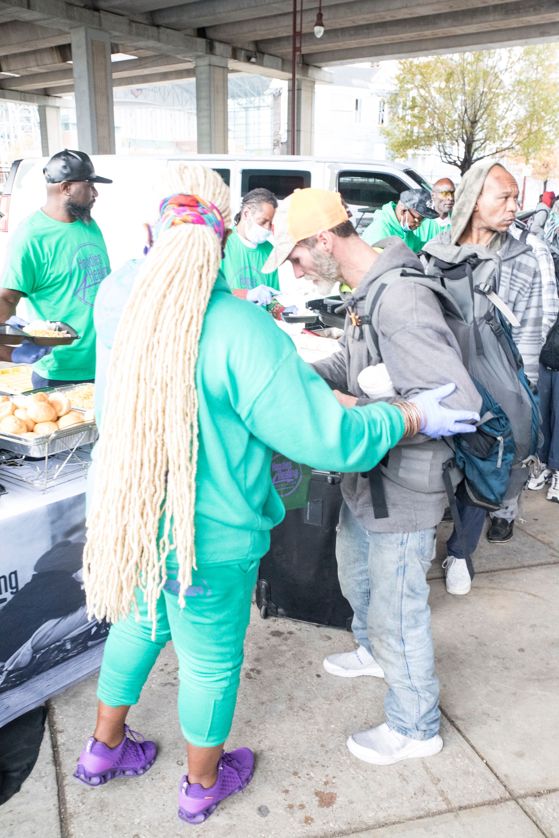 A woman in a green sweatshirt is helping a man with his backpack.