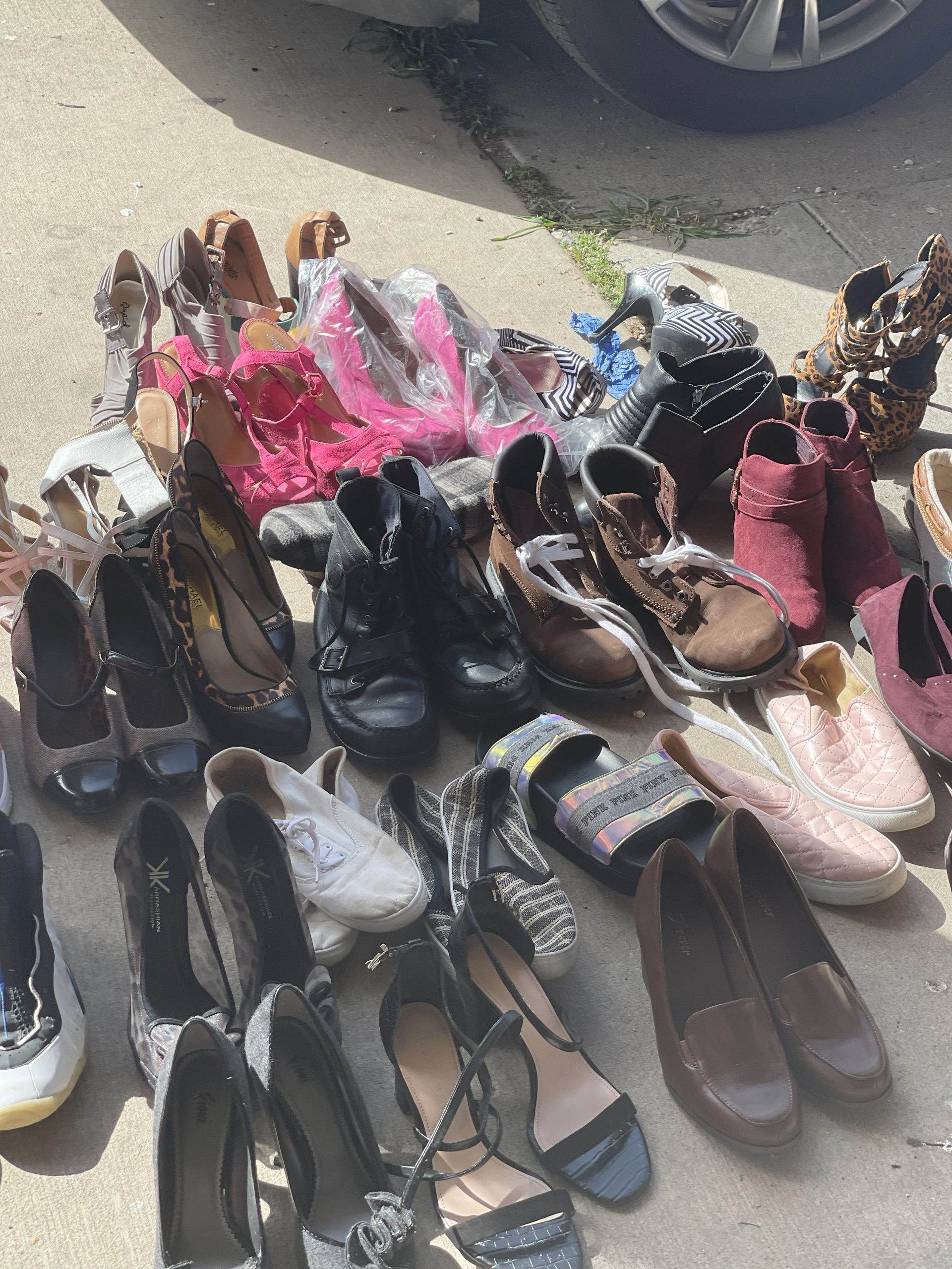 A bunch of shoes are sitting on the ground in front of a car.