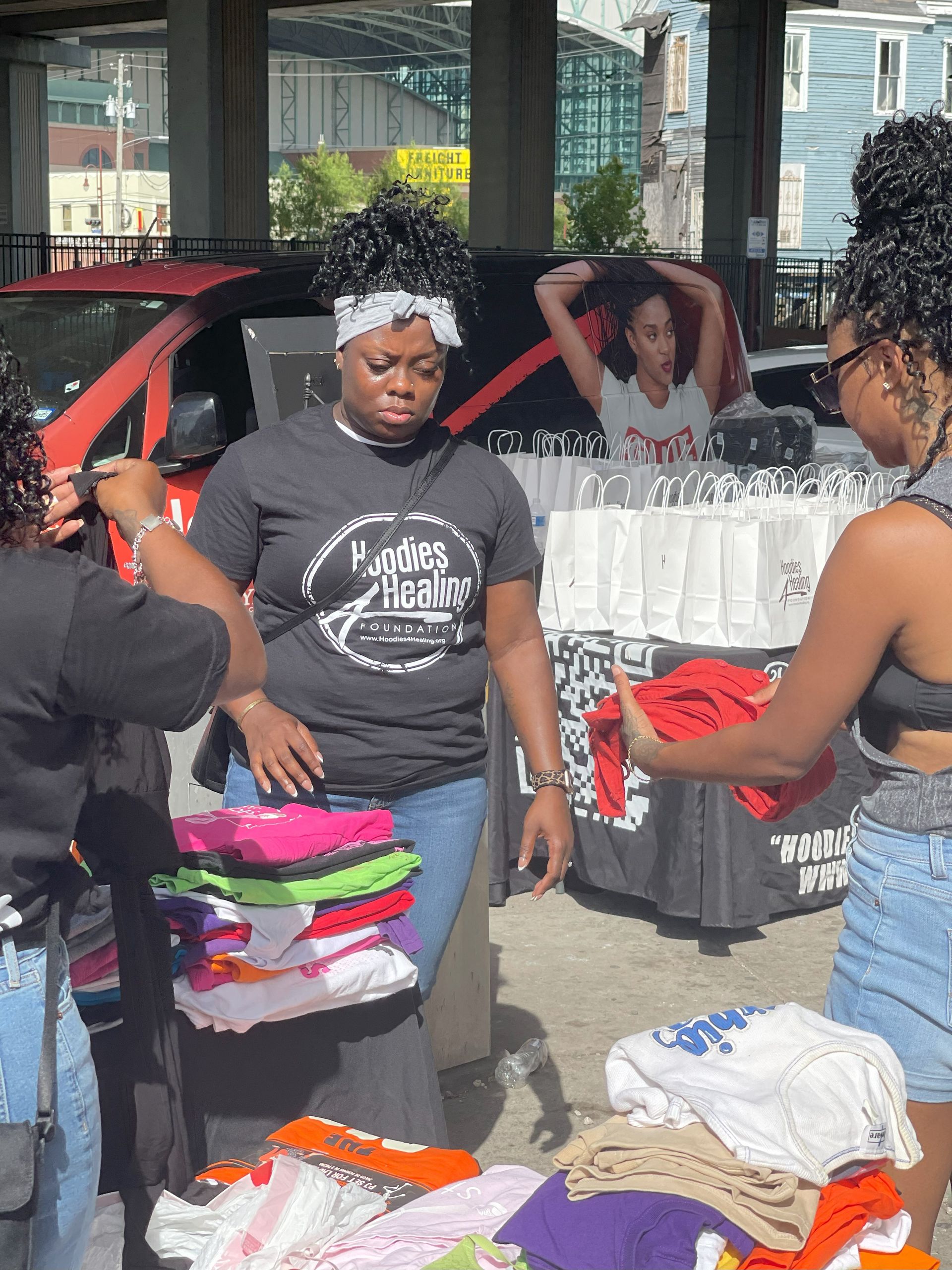 Two women are standing in front of a table with clothes on it.