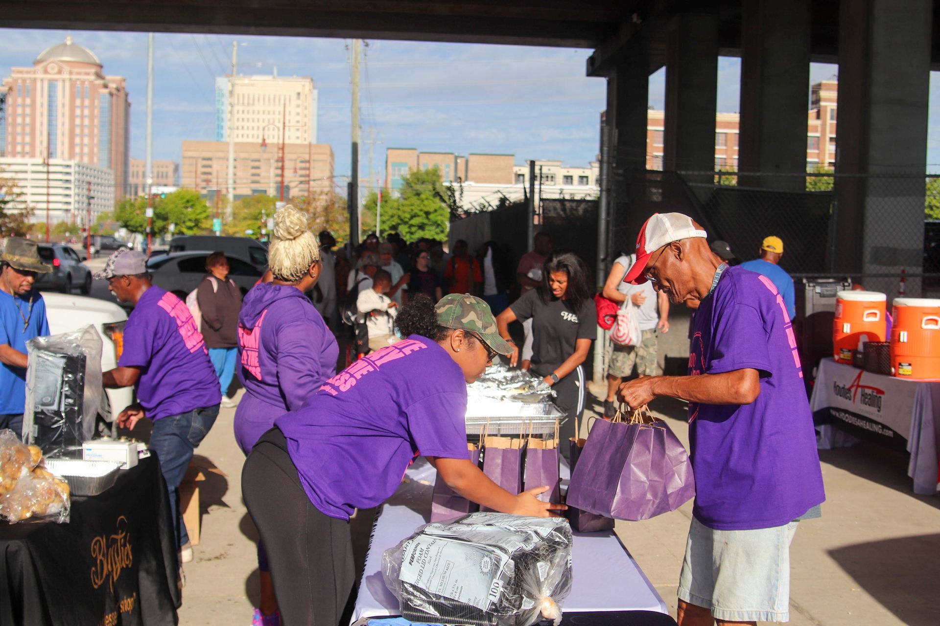 A group of people in purple shirts are standing around a table.