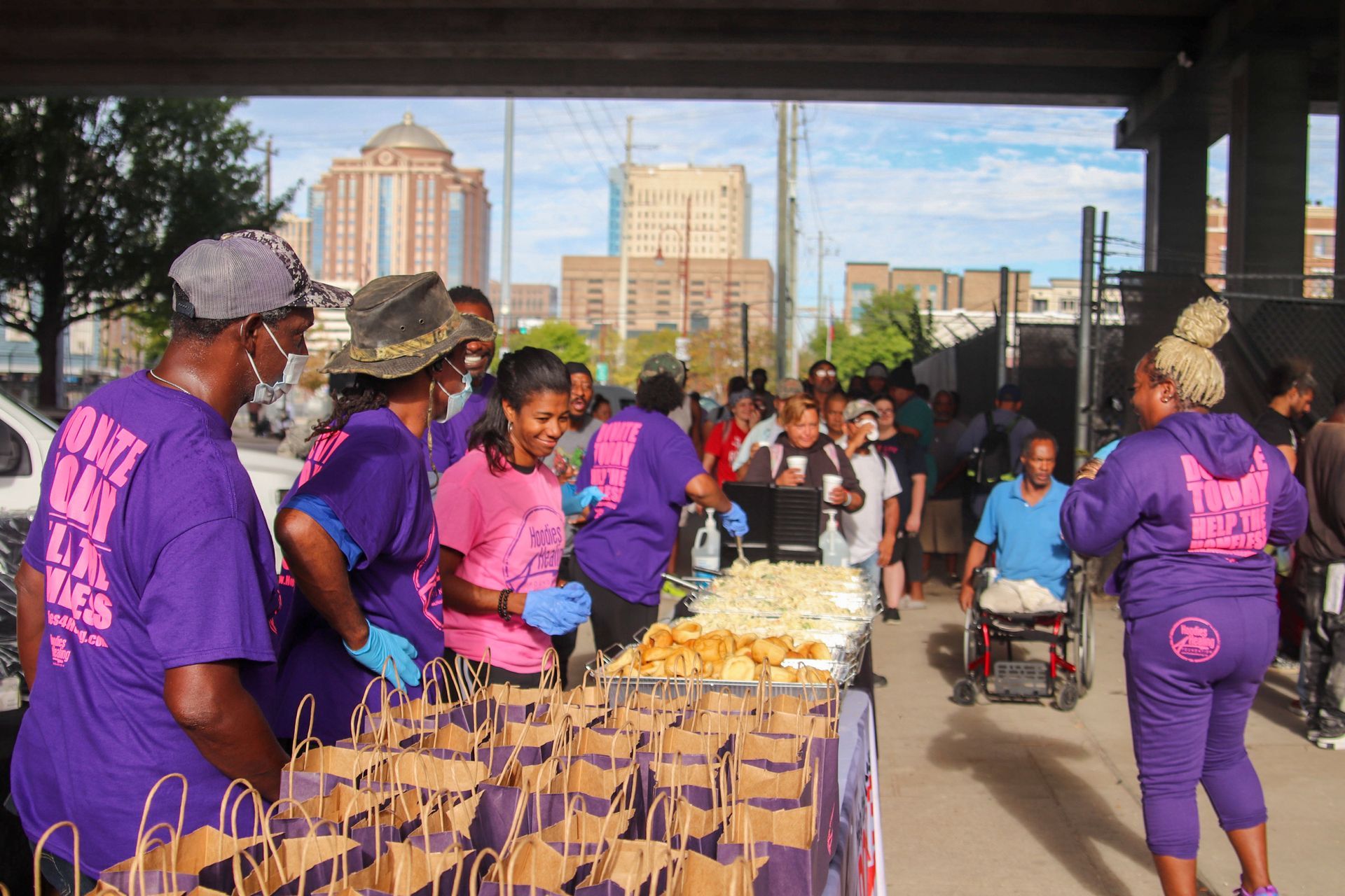 A group of people are standing around a table with bags of food.
