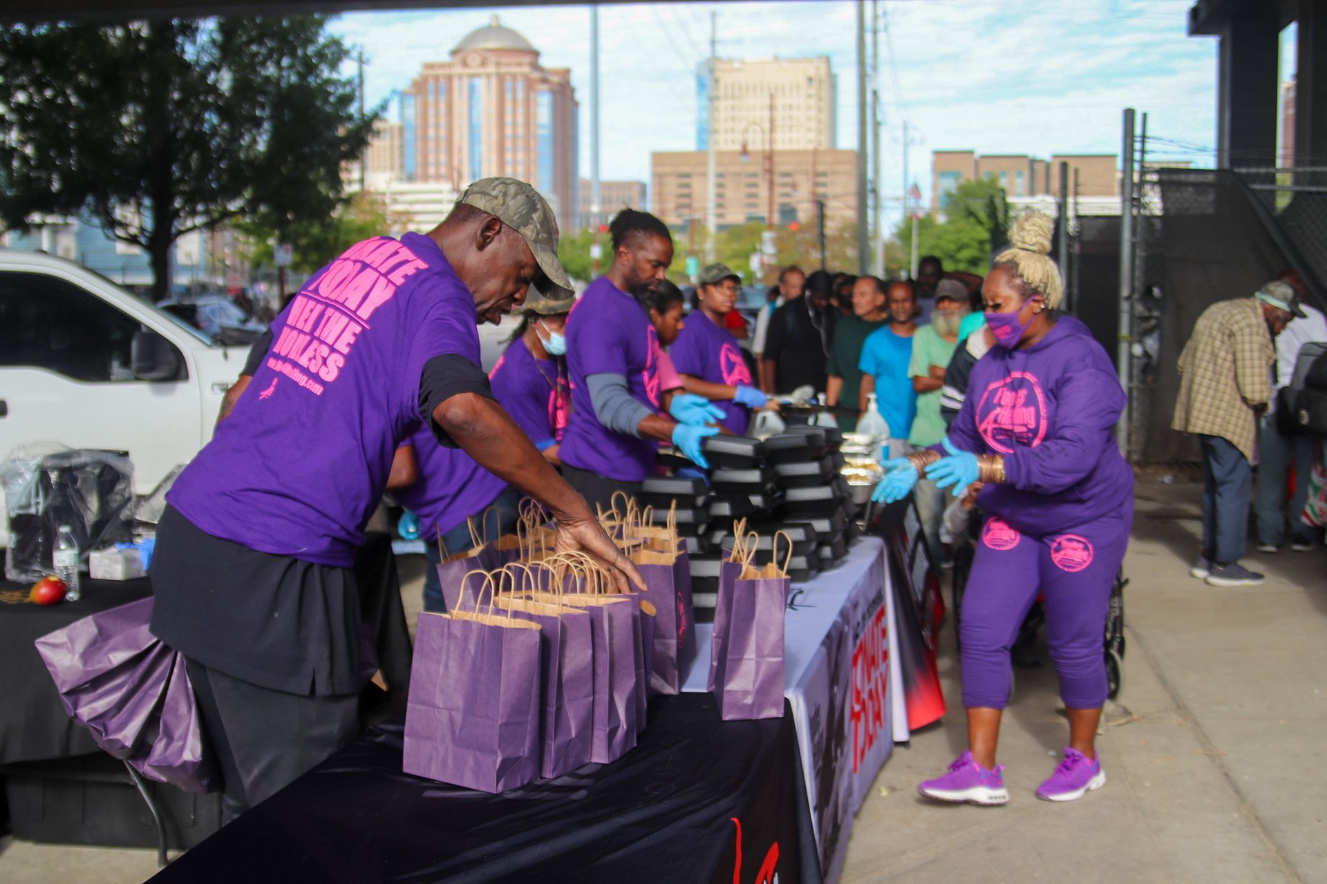 A group of people standing around a table with purple bags on it
