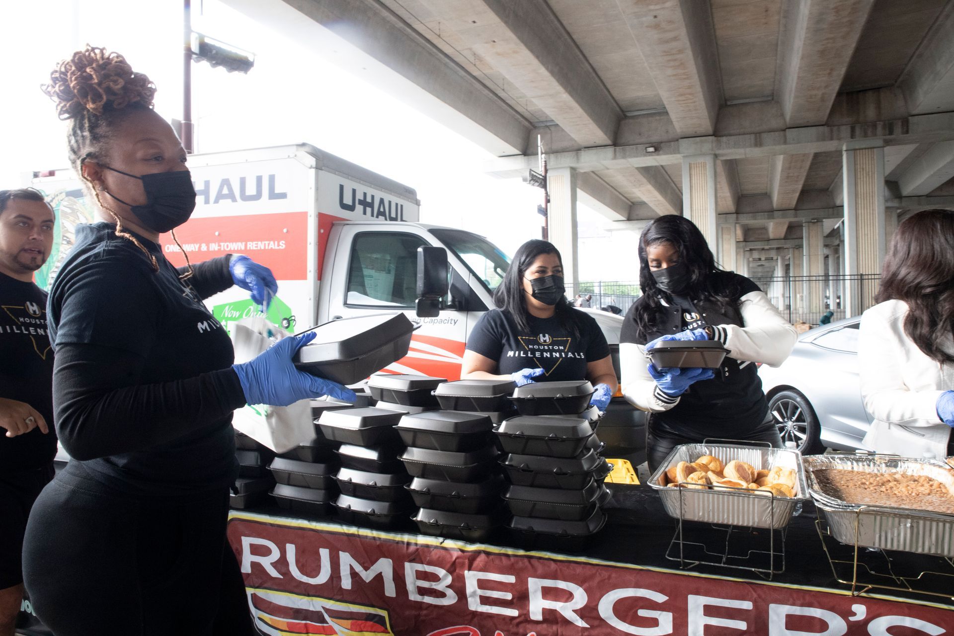 A woman wearing a mask is standing in front of a rumberger 's food stand.
