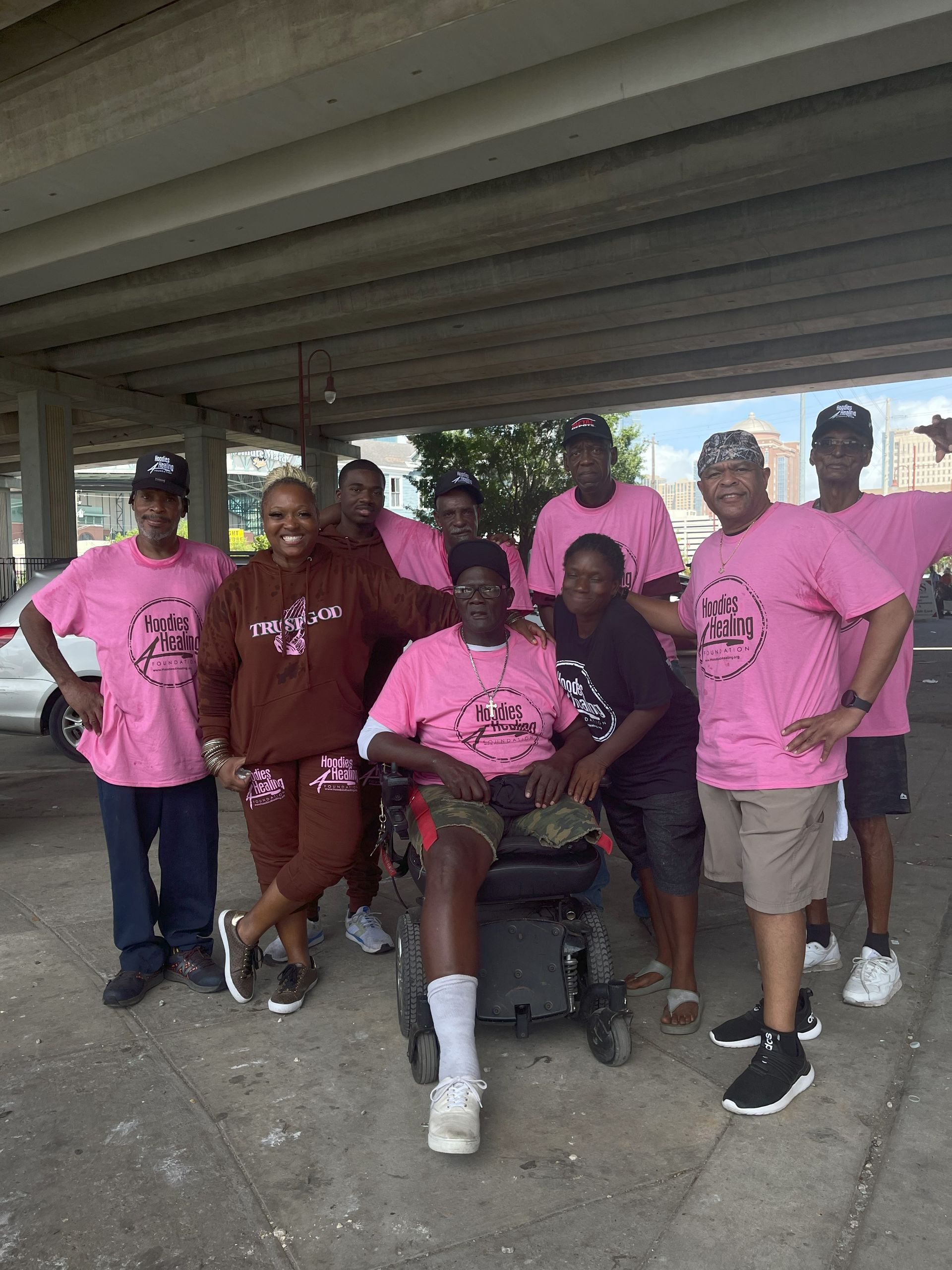 A group of people wearing pink shirts are posing for a picture with a man in a wheelchair.