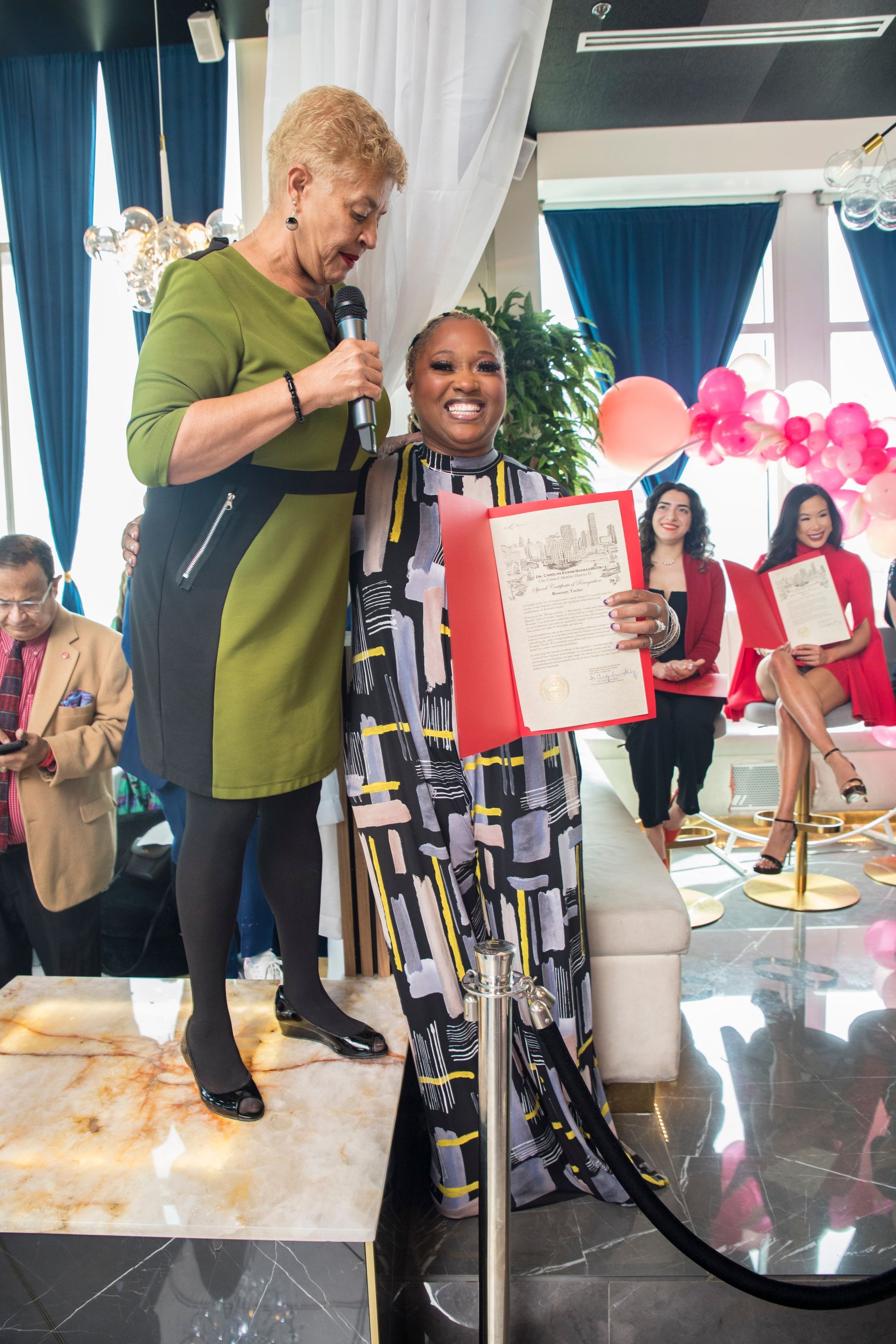 Two women are standing next to each other on a stage holding a certificate.