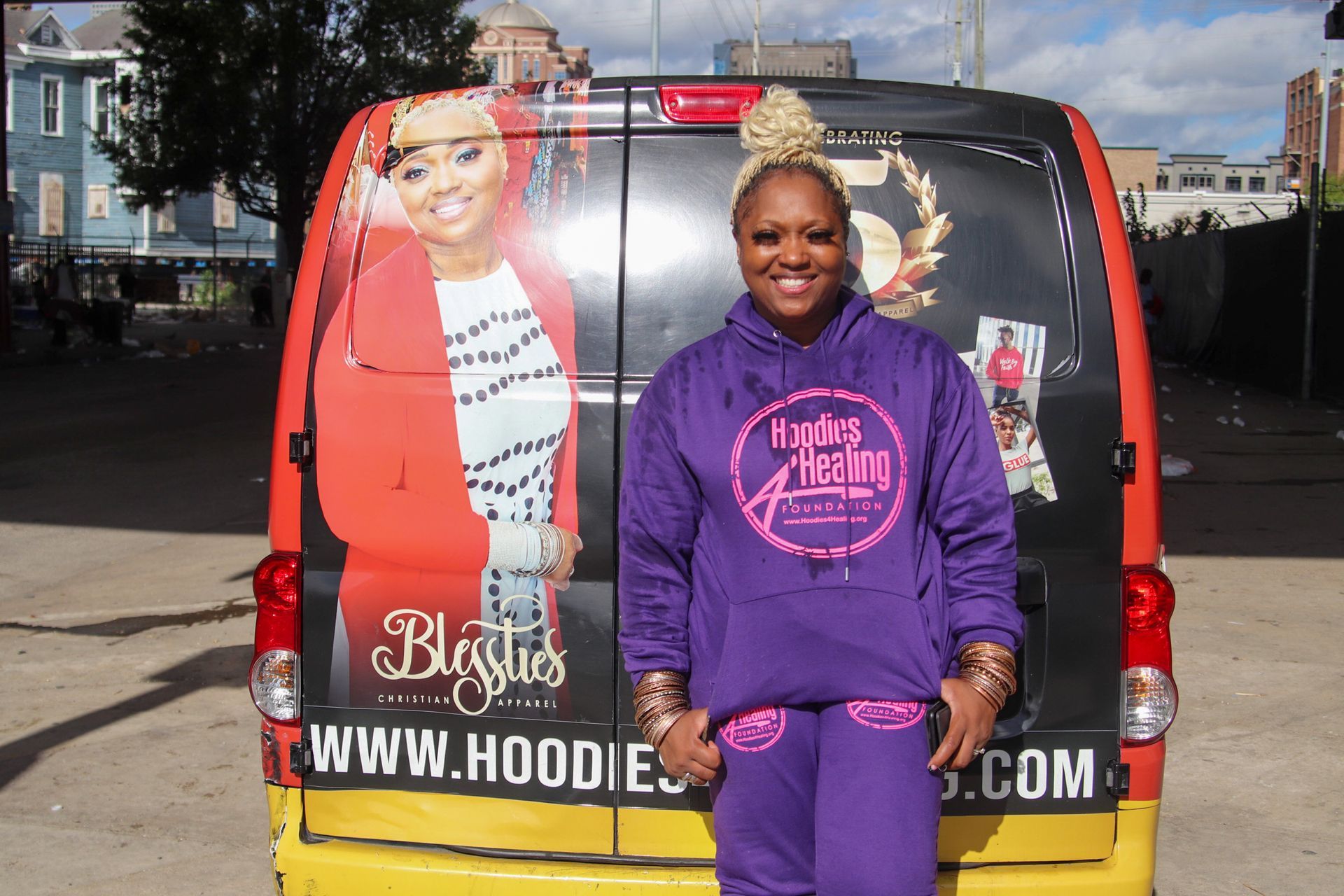 A woman in a purple hoodie stands in front of a van that says www.hoodies.com