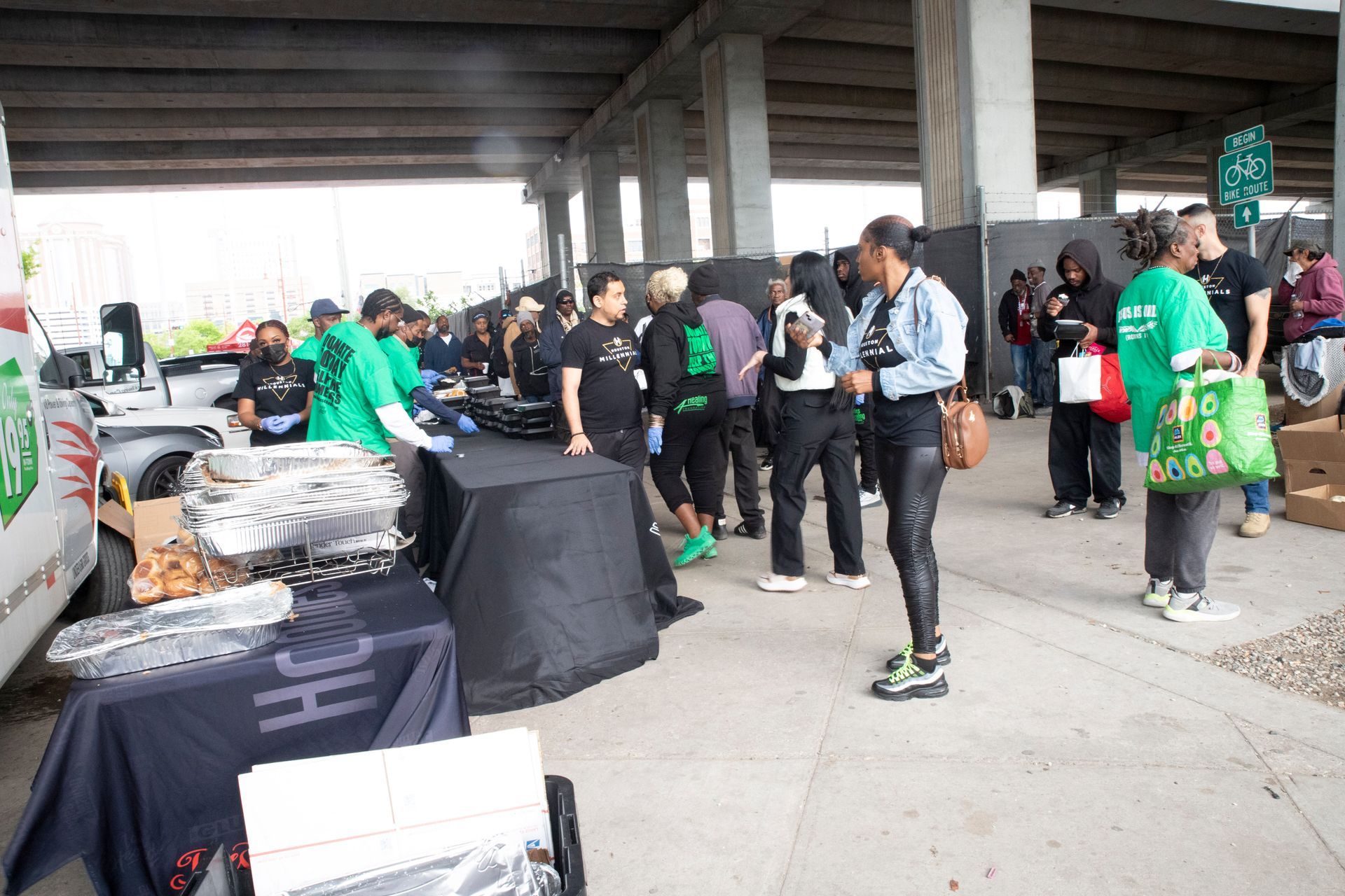 A group of people are standing around tables under a bridge.