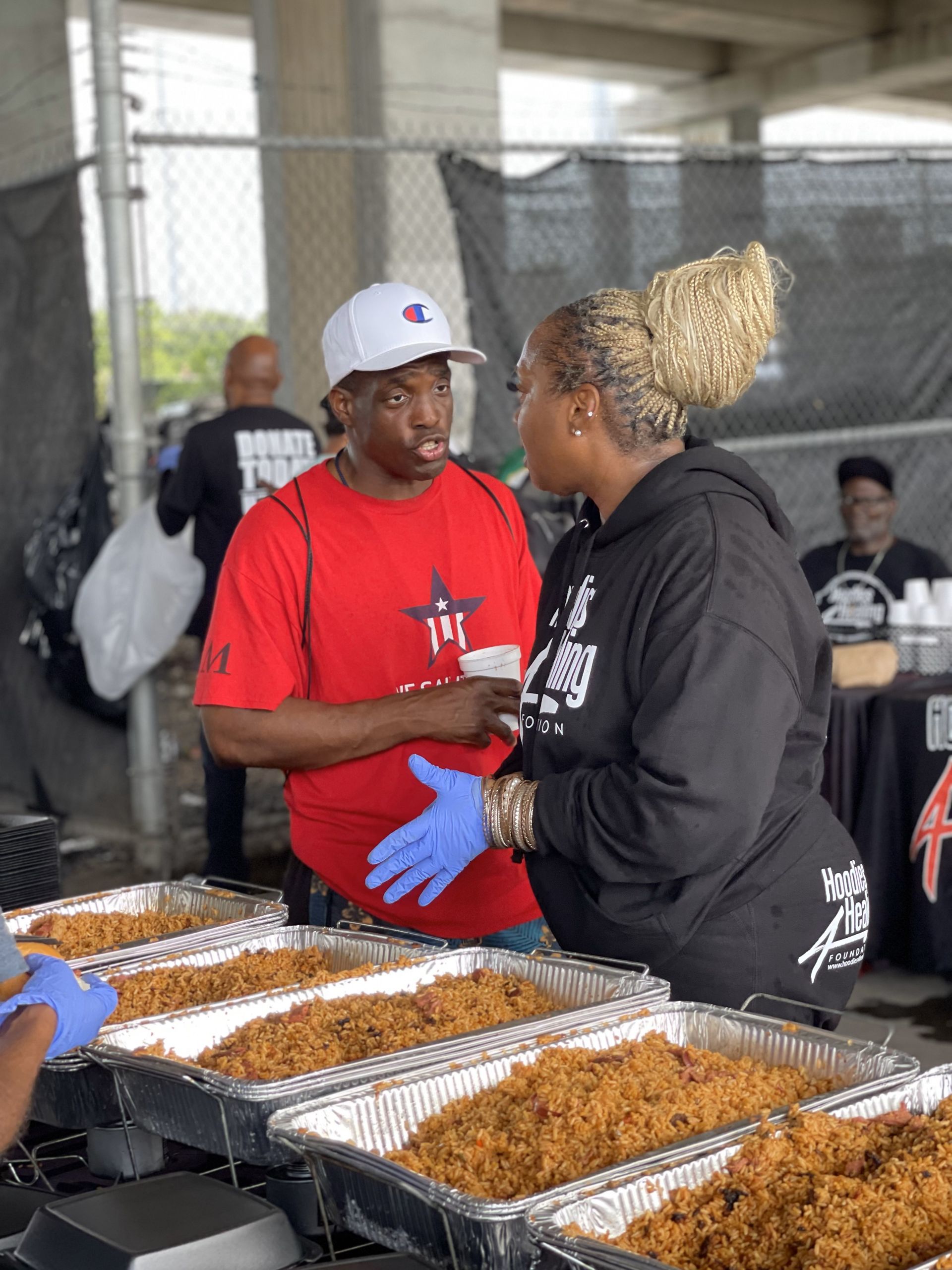 A man and a woman are standing in front of a table with trays of food.