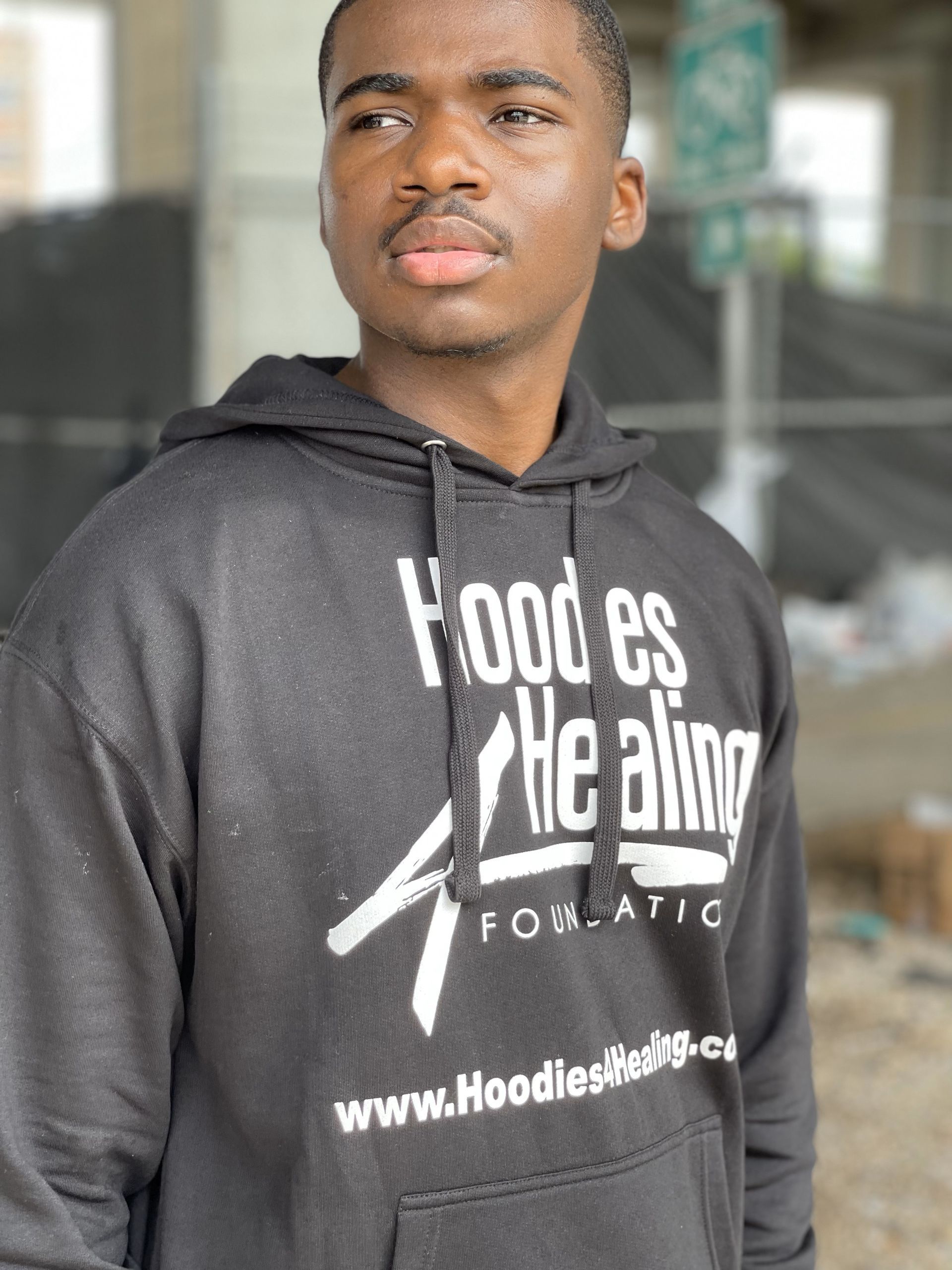 A young man wearing a black hoodie that says hood es the aiming