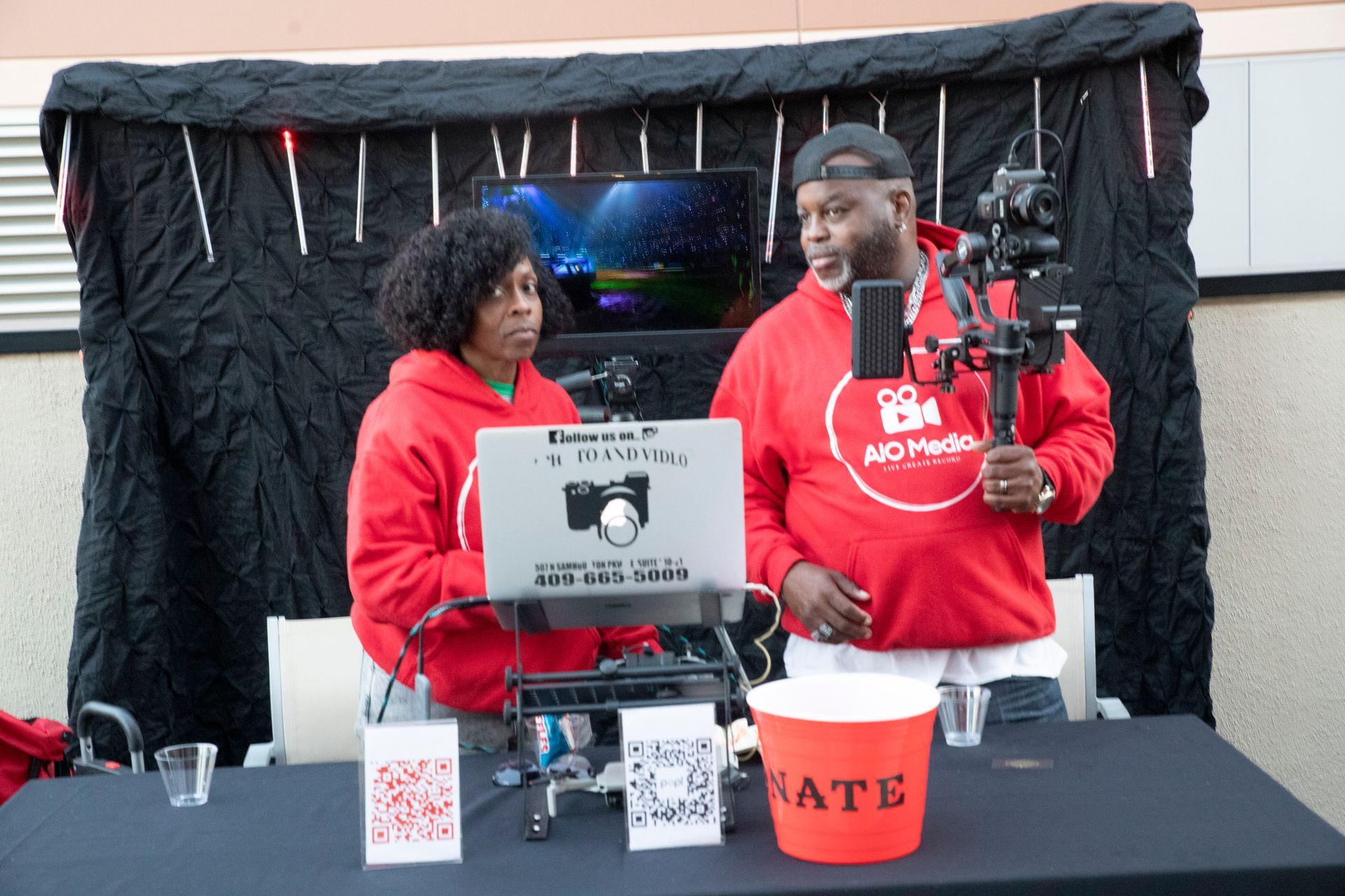 A man and a woman are standing at a table with a laptop and a microphone.