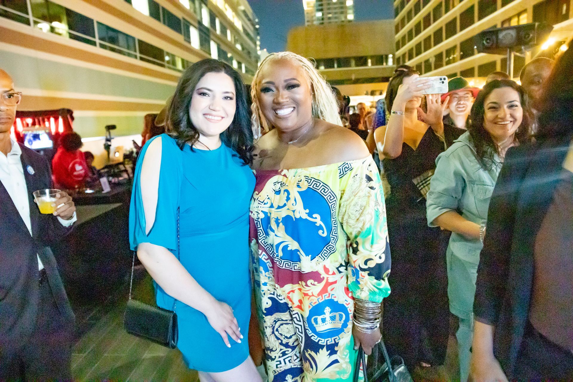 Two women are posing for a picture in front of a crowd of people.