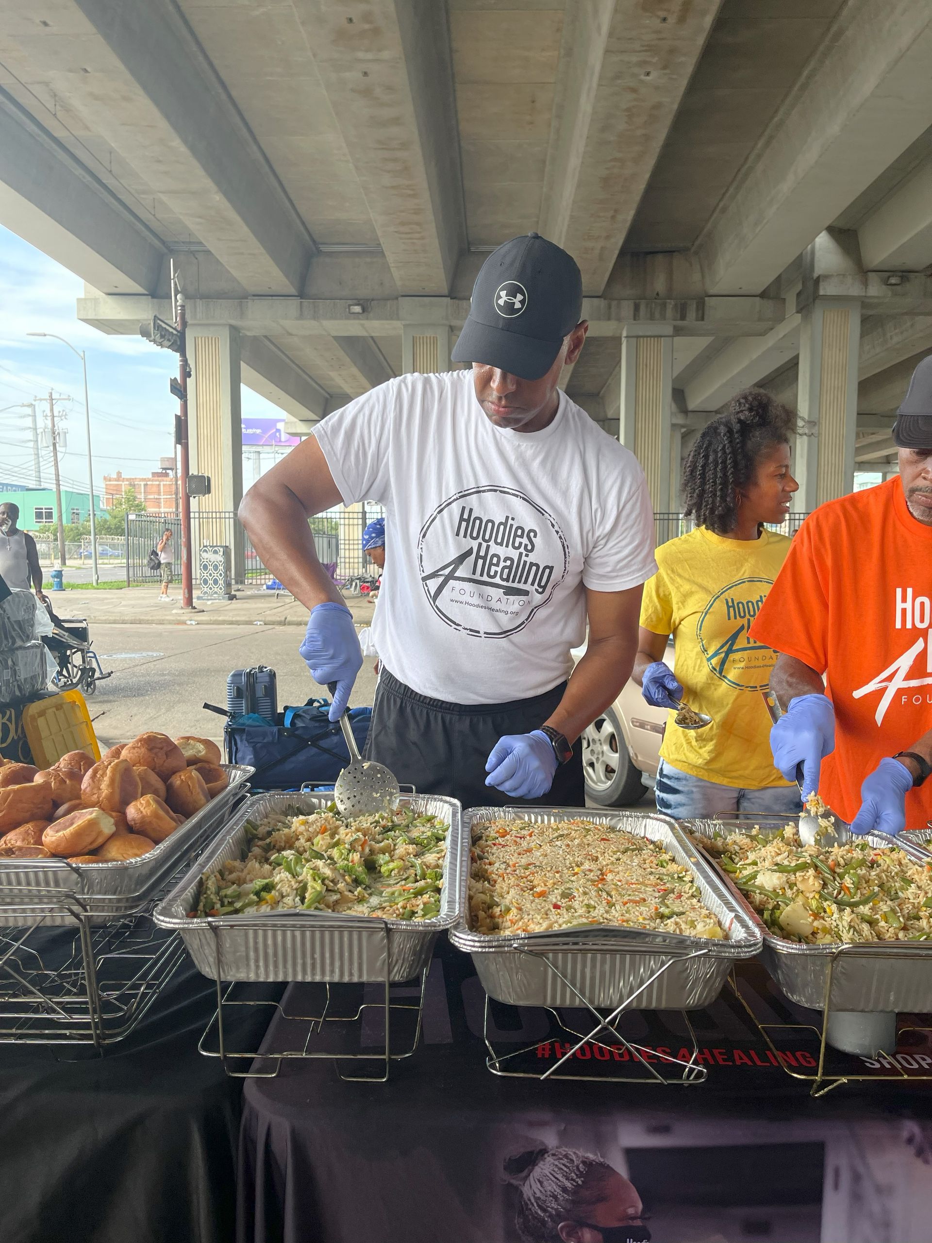 A man in a white shirt is preparing food on a table under a bridge.