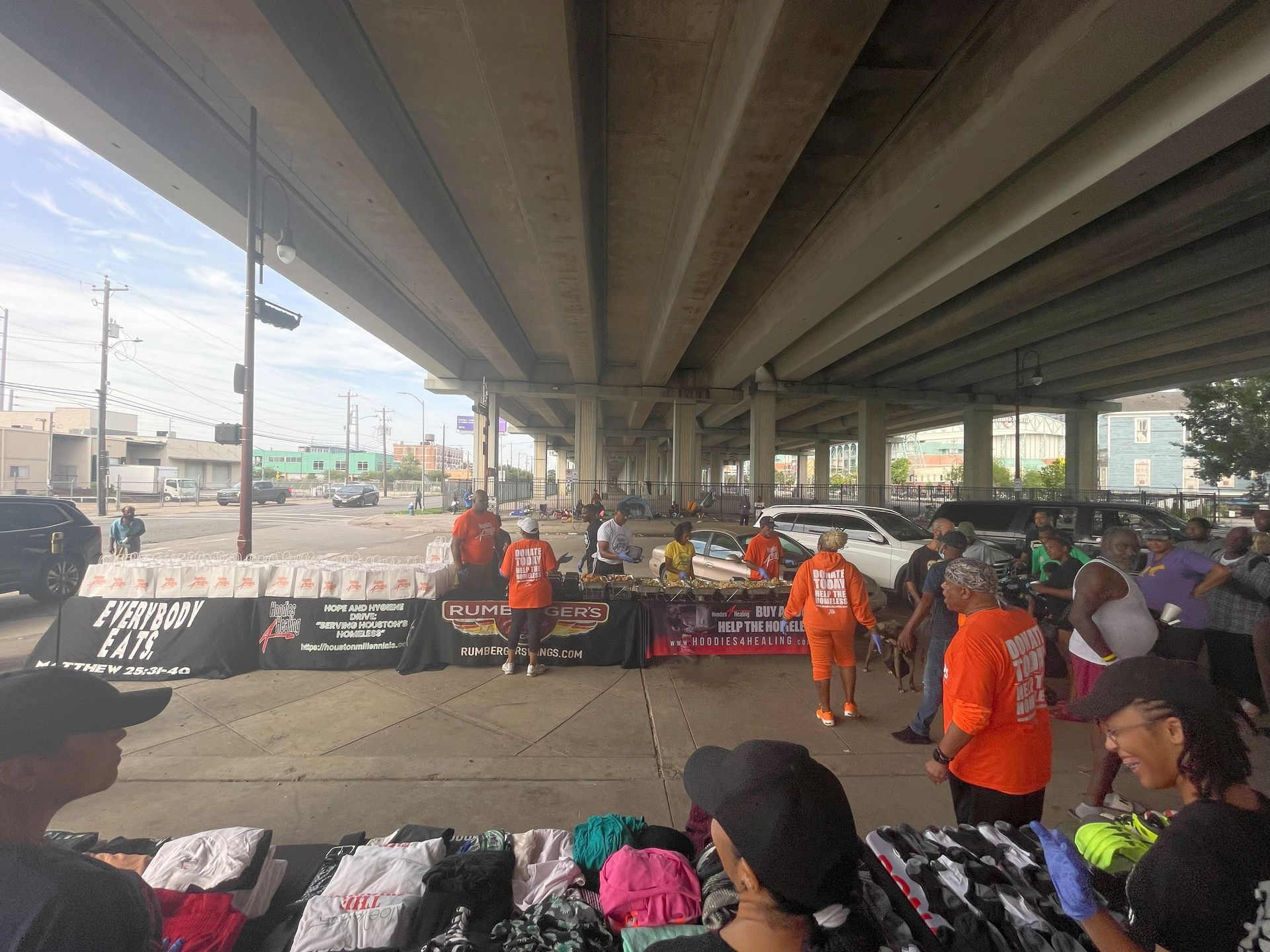 A group of people are standing around a table under a bridge.