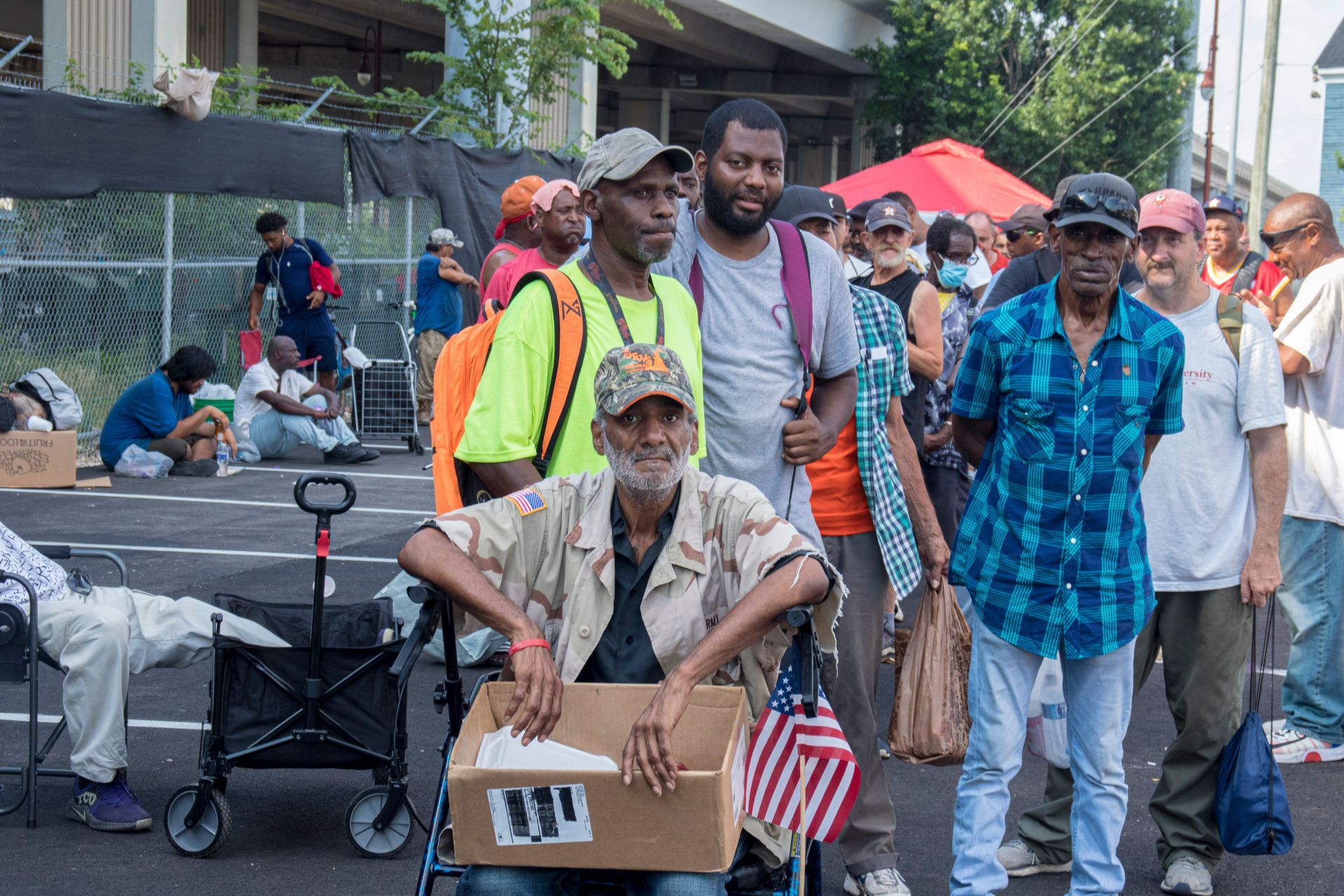 A group of people are standing around a man in a wheelchair holding an american flag.