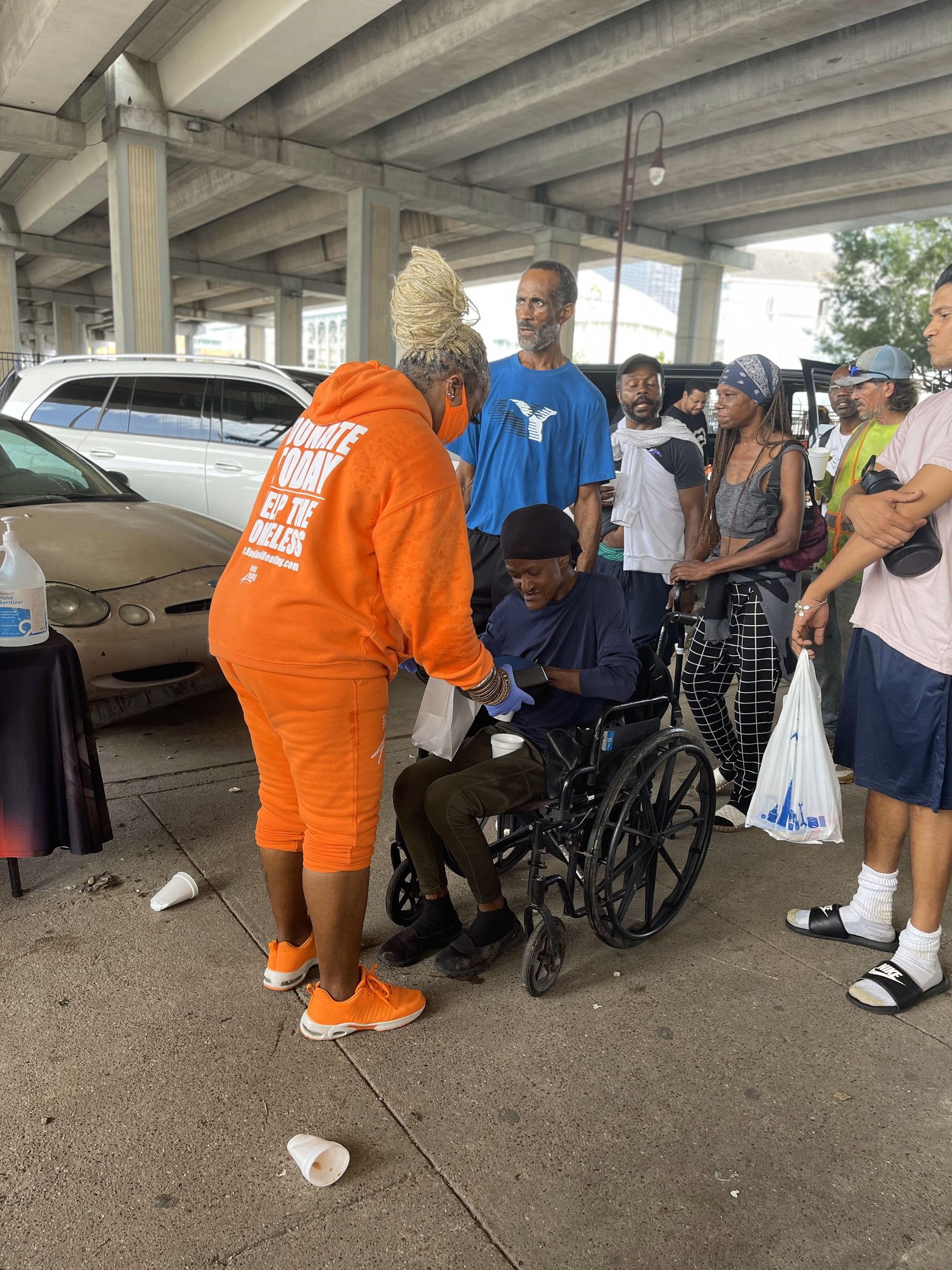 A woman in an orange hoodie is helping a man in a wheelchair.