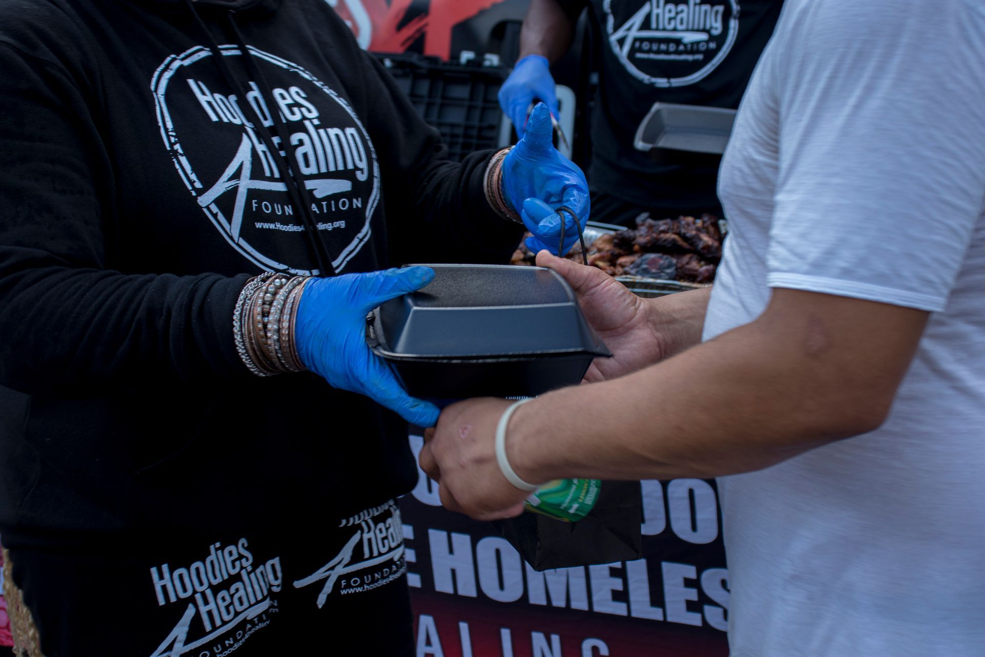 A person wearing blue gloves is giving a container of food to another person.