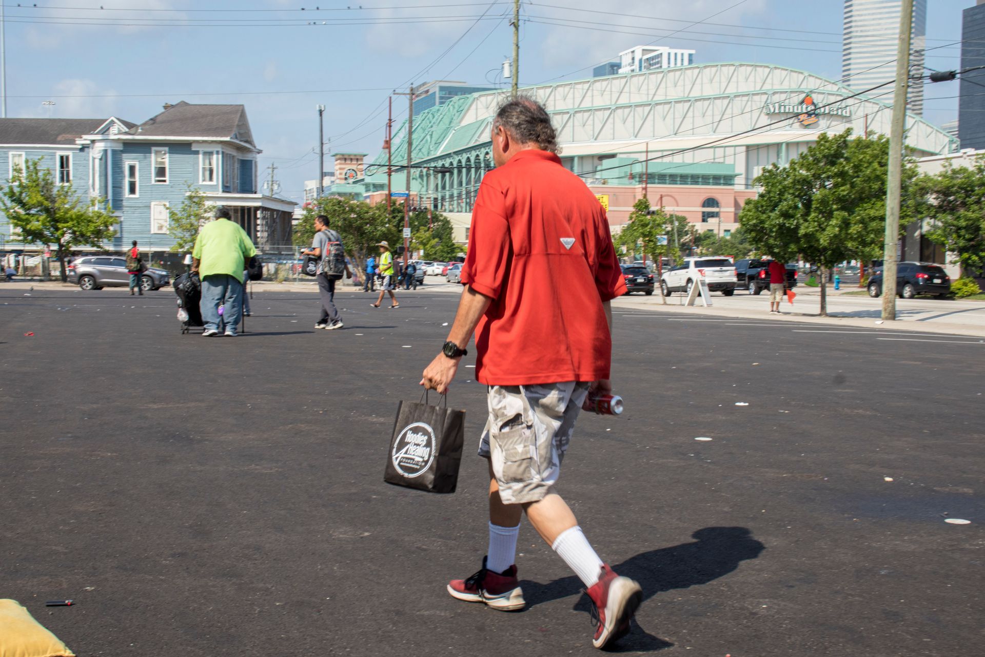 A man in a red shirt is walking down the street holding a bag.