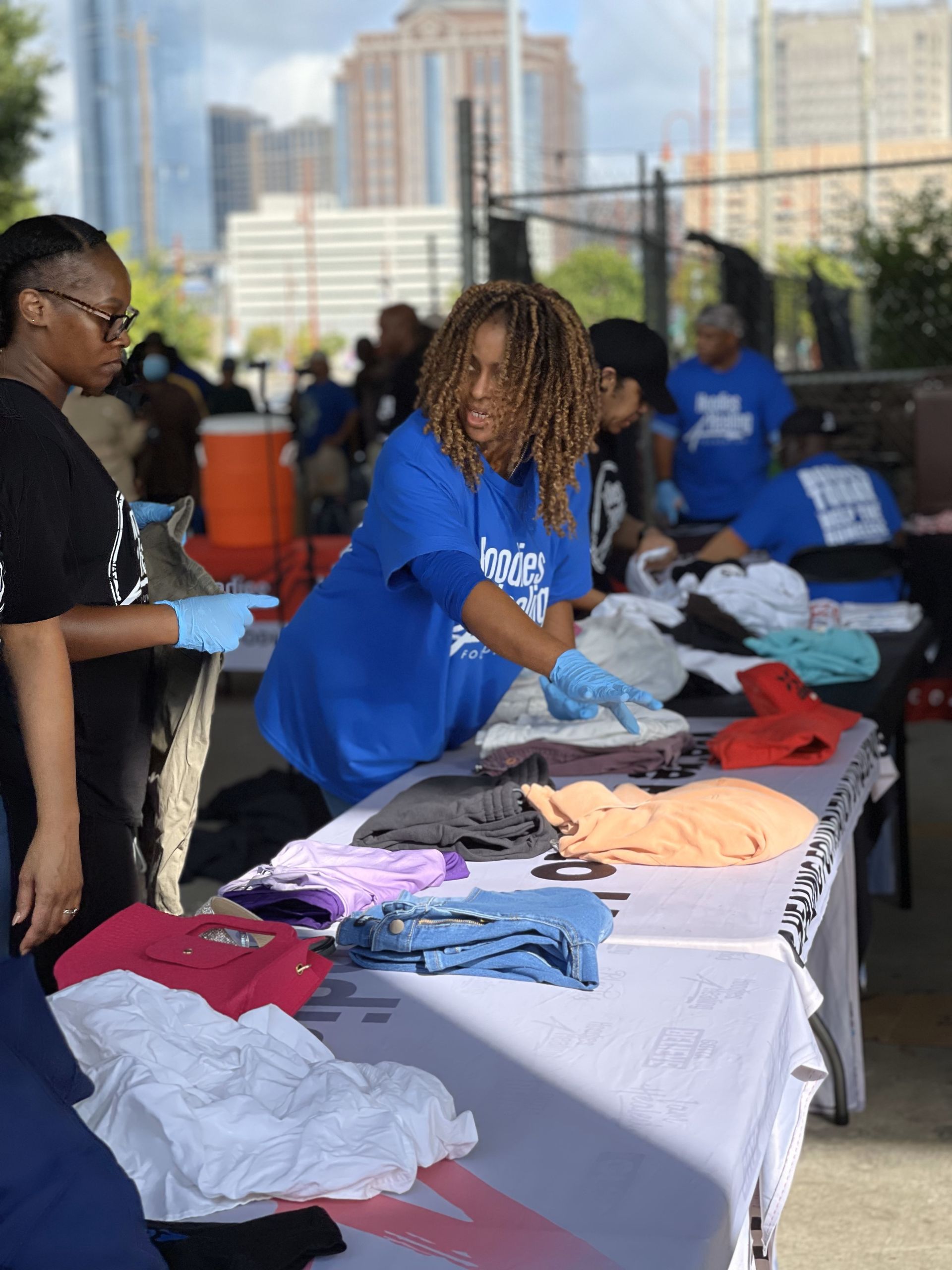 A woman in a blue shirt is standing at a table with clothes on it.