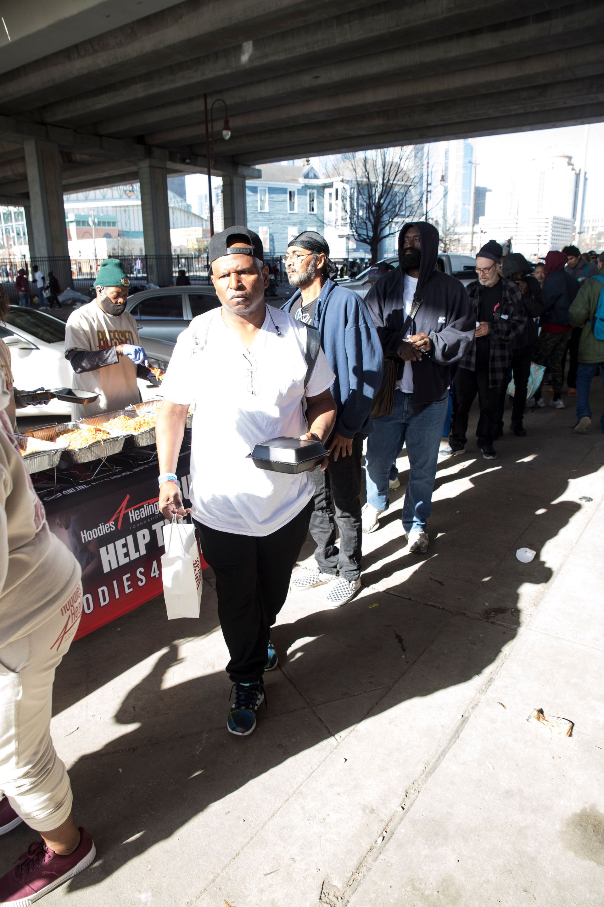 A group of people are walking down a sidewalk under a bridge.
