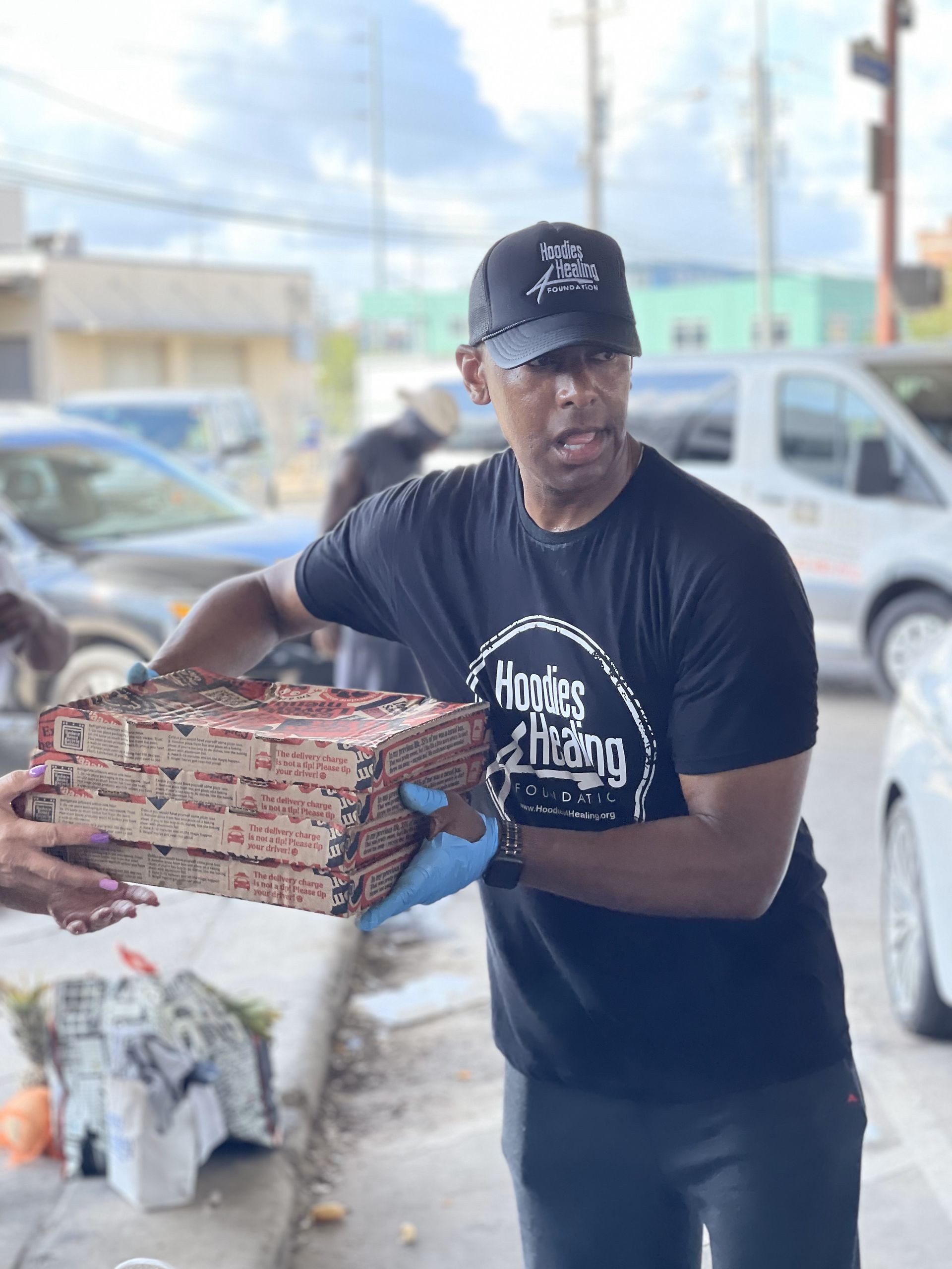 A man in a black shirt is carrying a stack of pizza boxes.