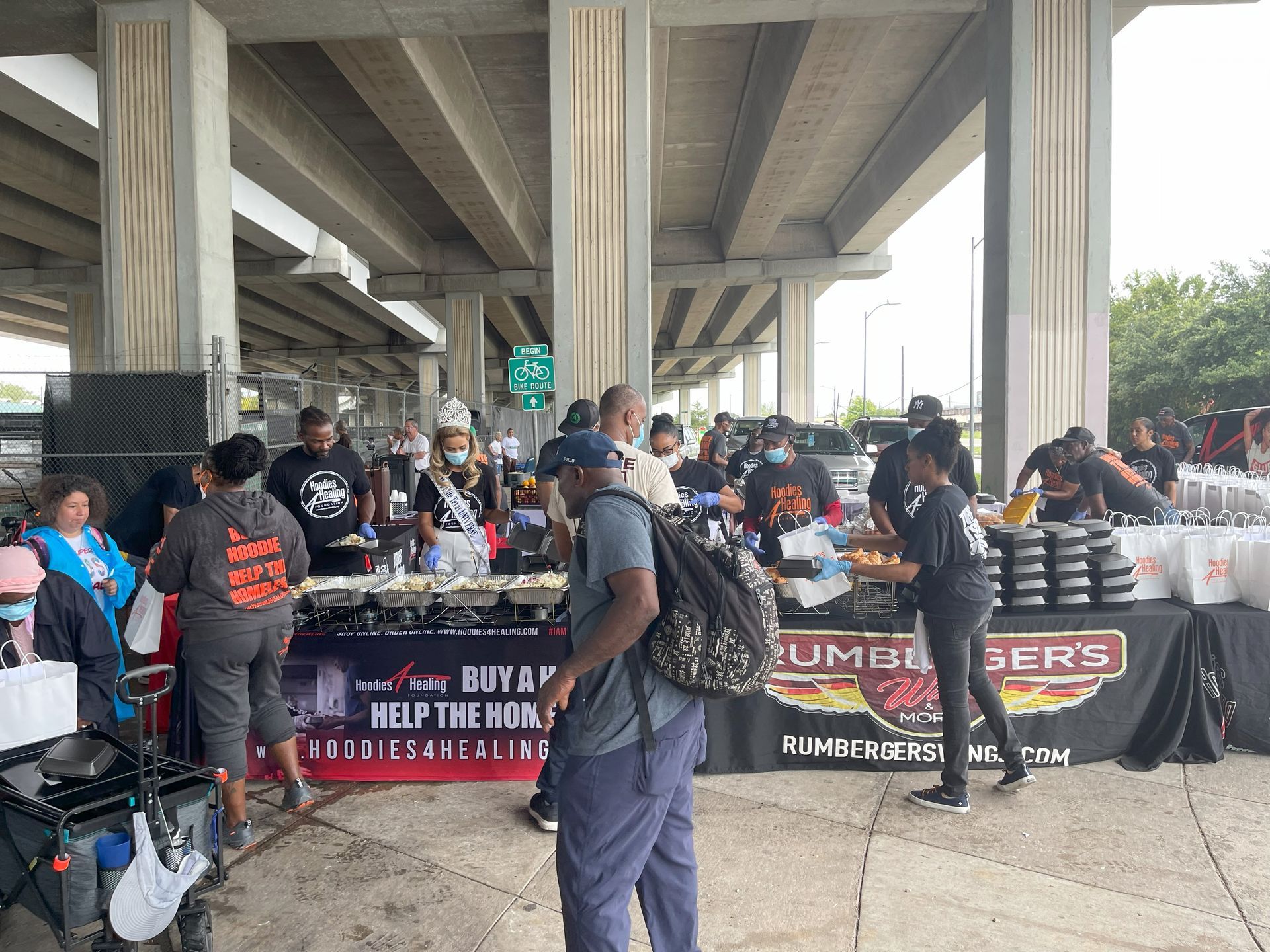 A group of people are standing around a table under a bridge.