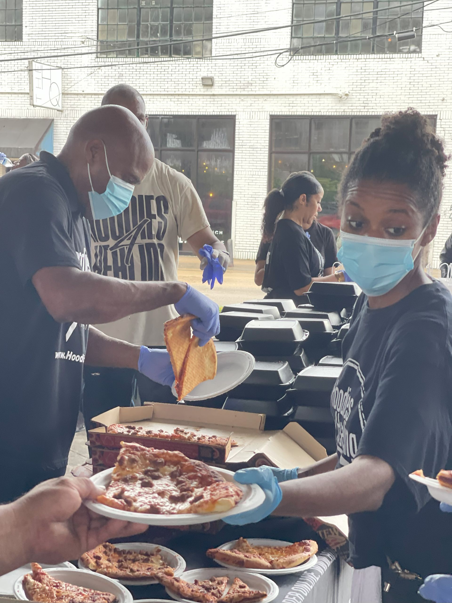 A woman wearing a mask is serving pizza to a group of people.