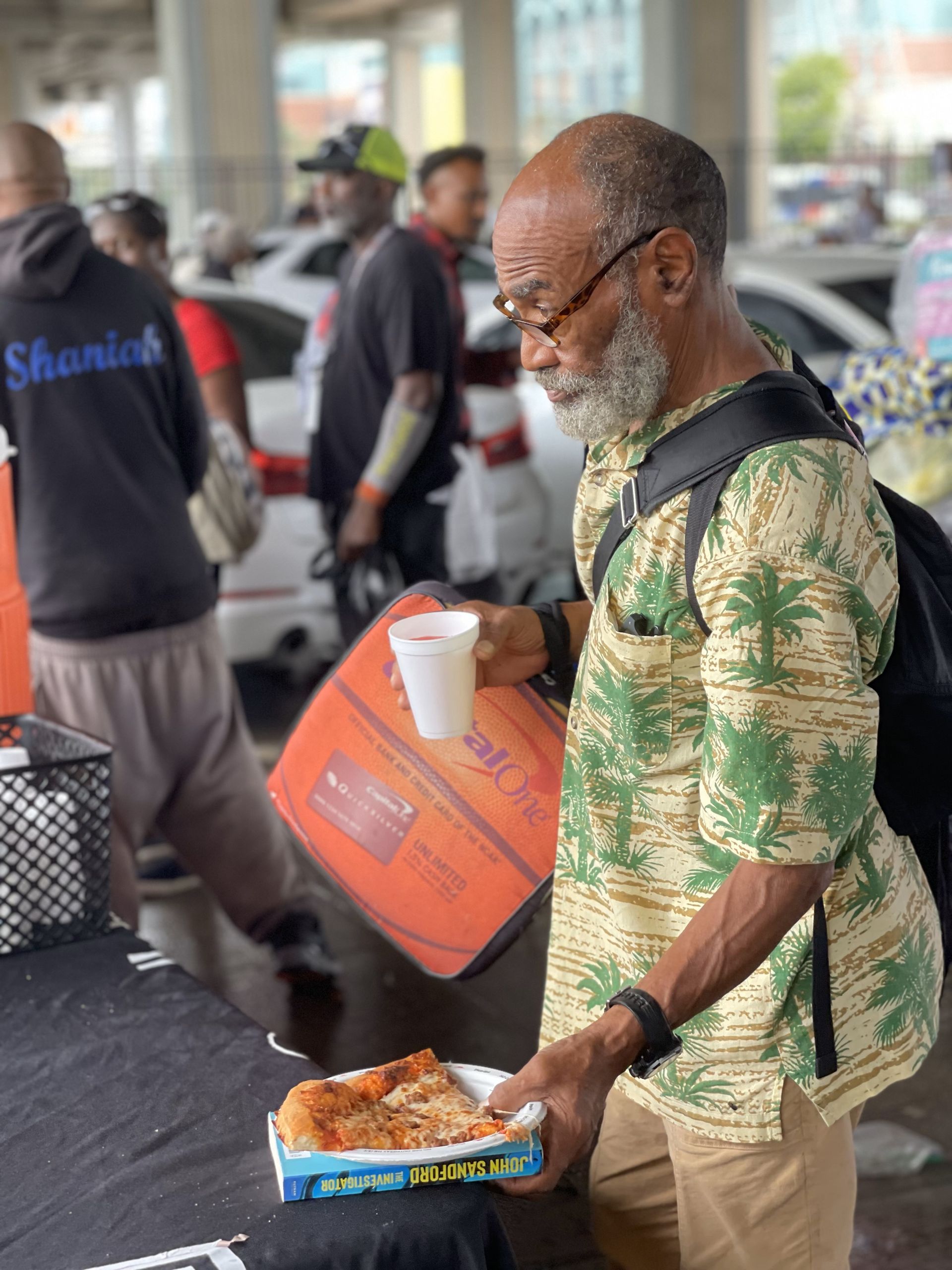 A man is holding a box of pizza and a cup of coffee.