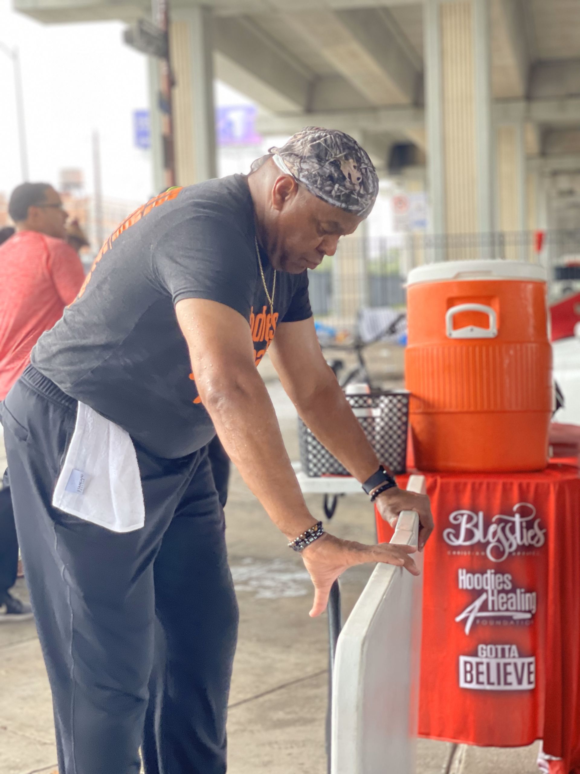 A man in a black shirt is standing next to an orange cooler.