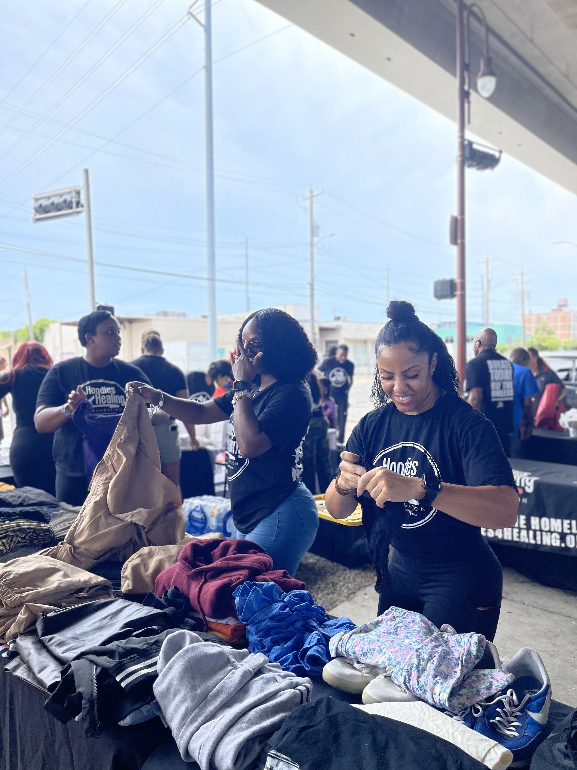 A group of people are standing around a table with clothes on it.