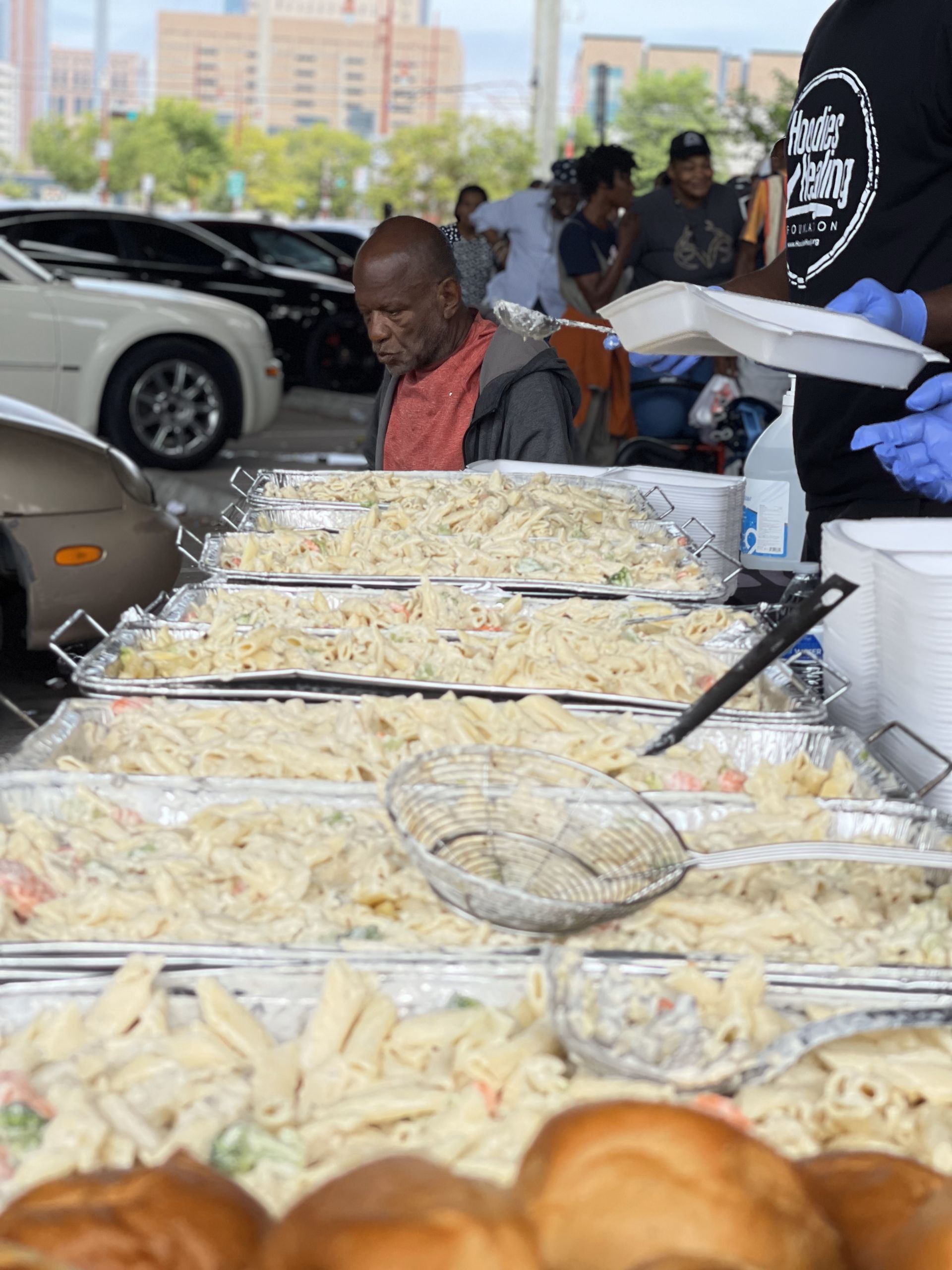 A man is serving food to a group of people in a parking lot.