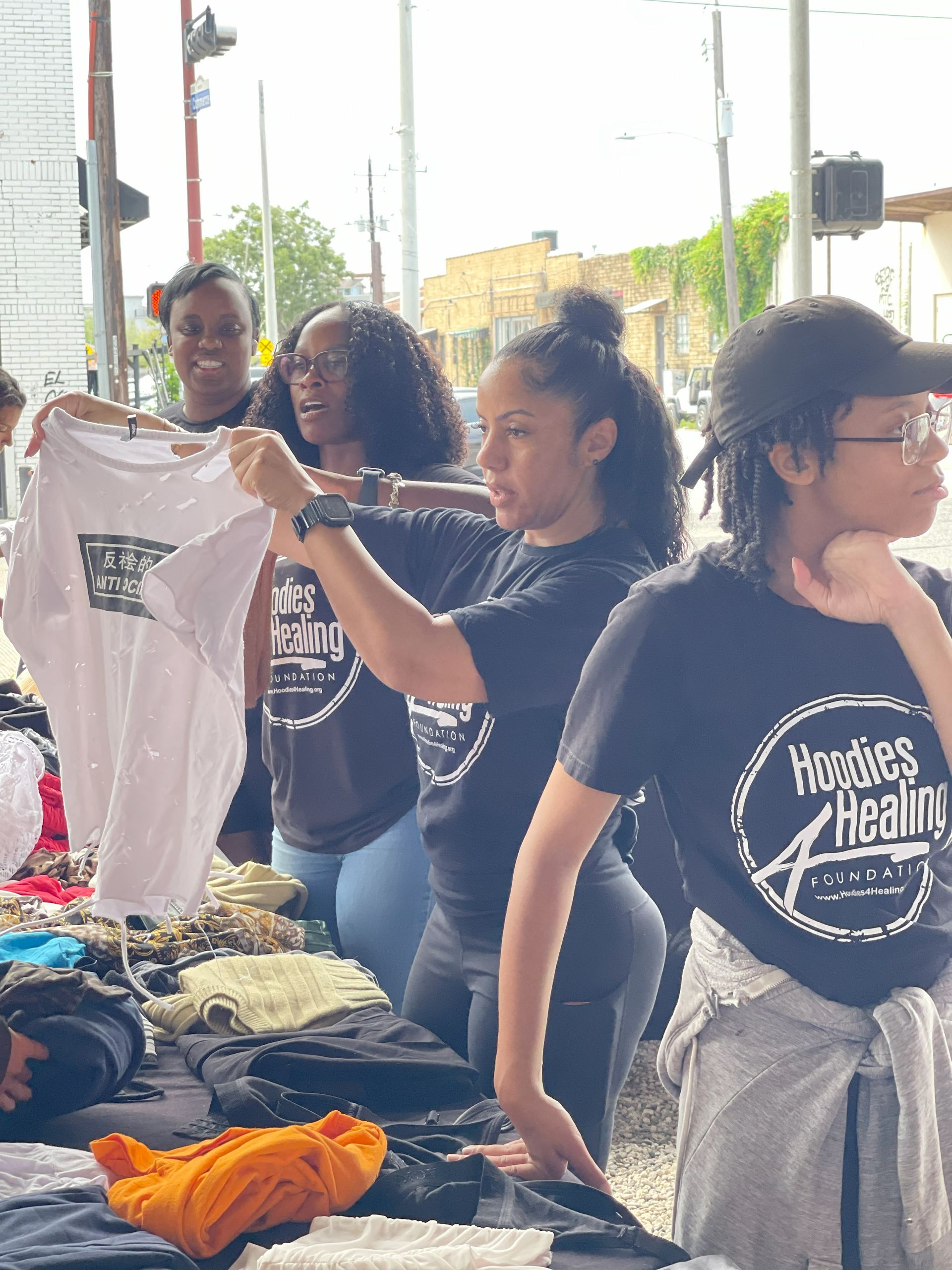A group of women wearing hoodies are standing around a table holding shirts.