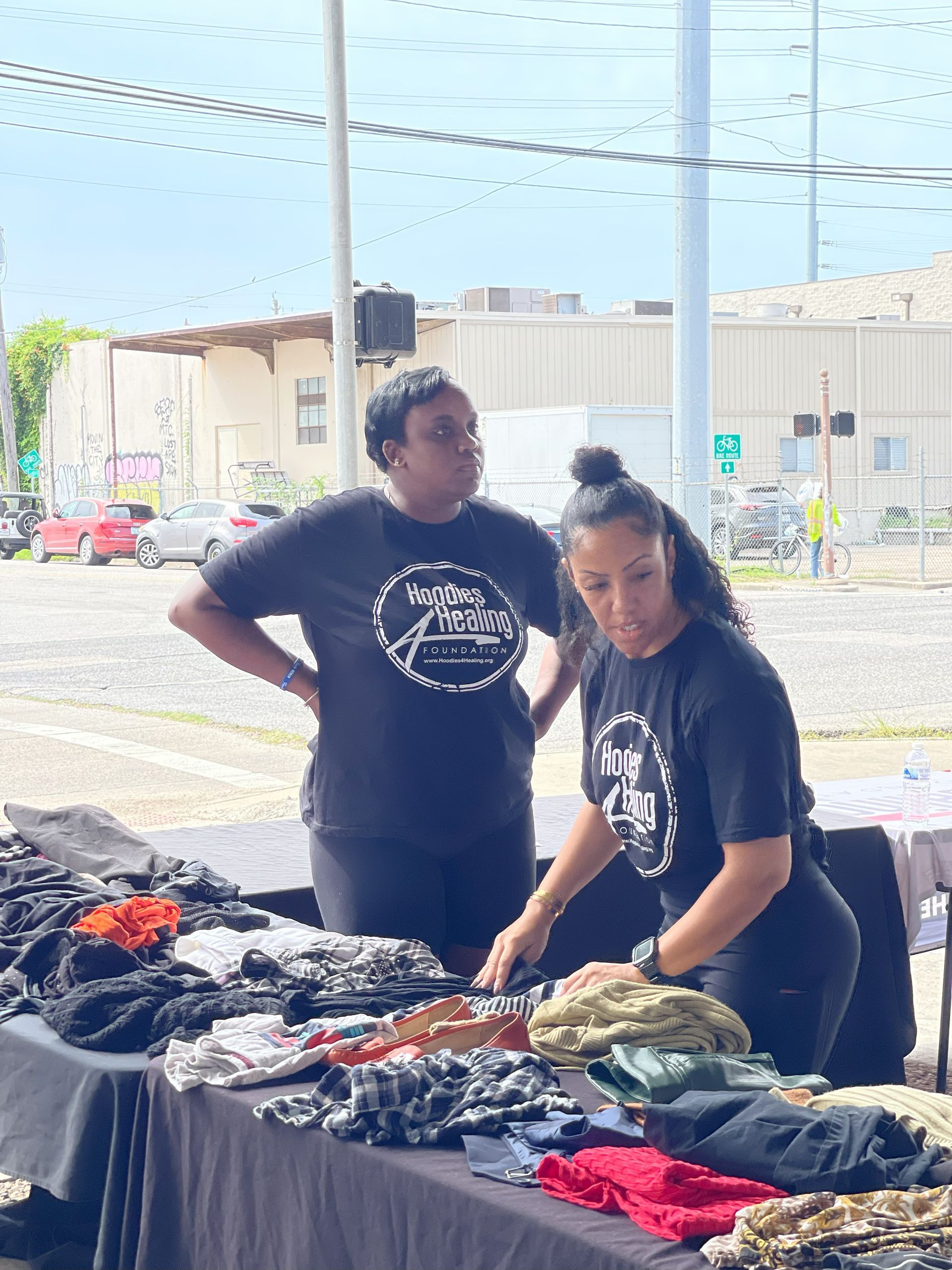 Two women are standing next to each other in front of a table full of clothes.