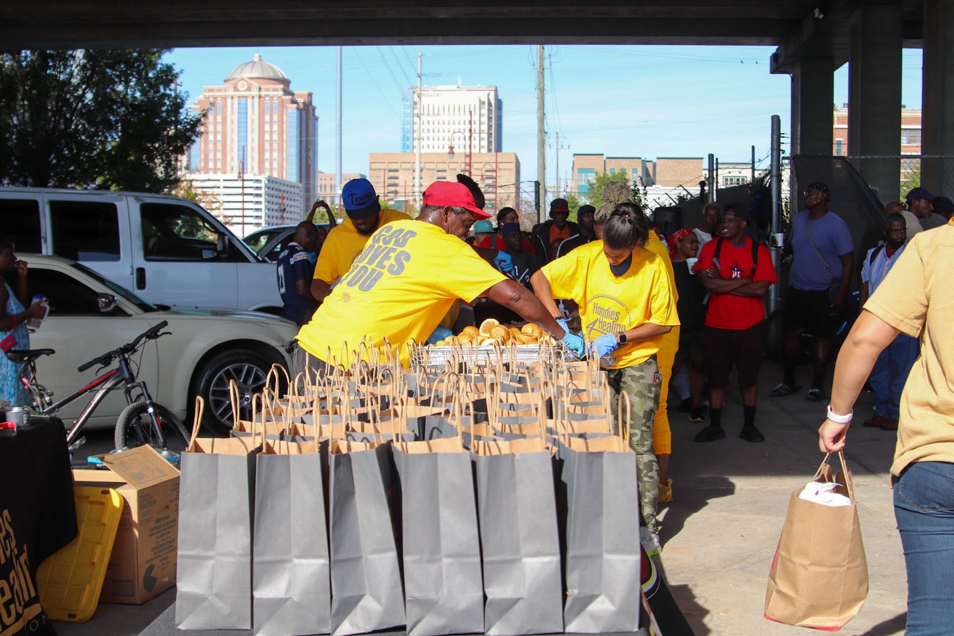 A group of people are gathered around a table with bags of food