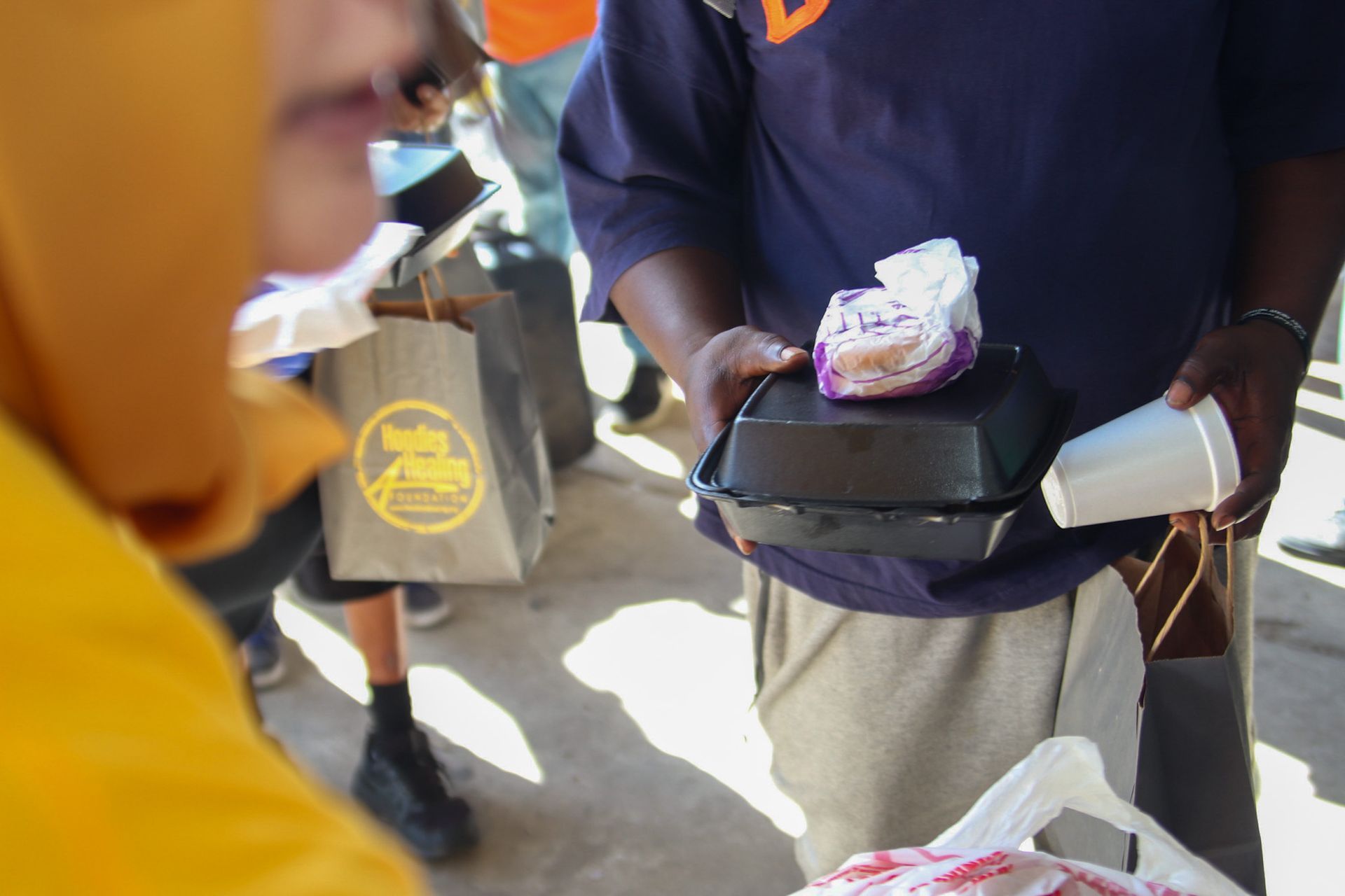 A man in a purple shirt is holding a styrofoam cup and a container of food.