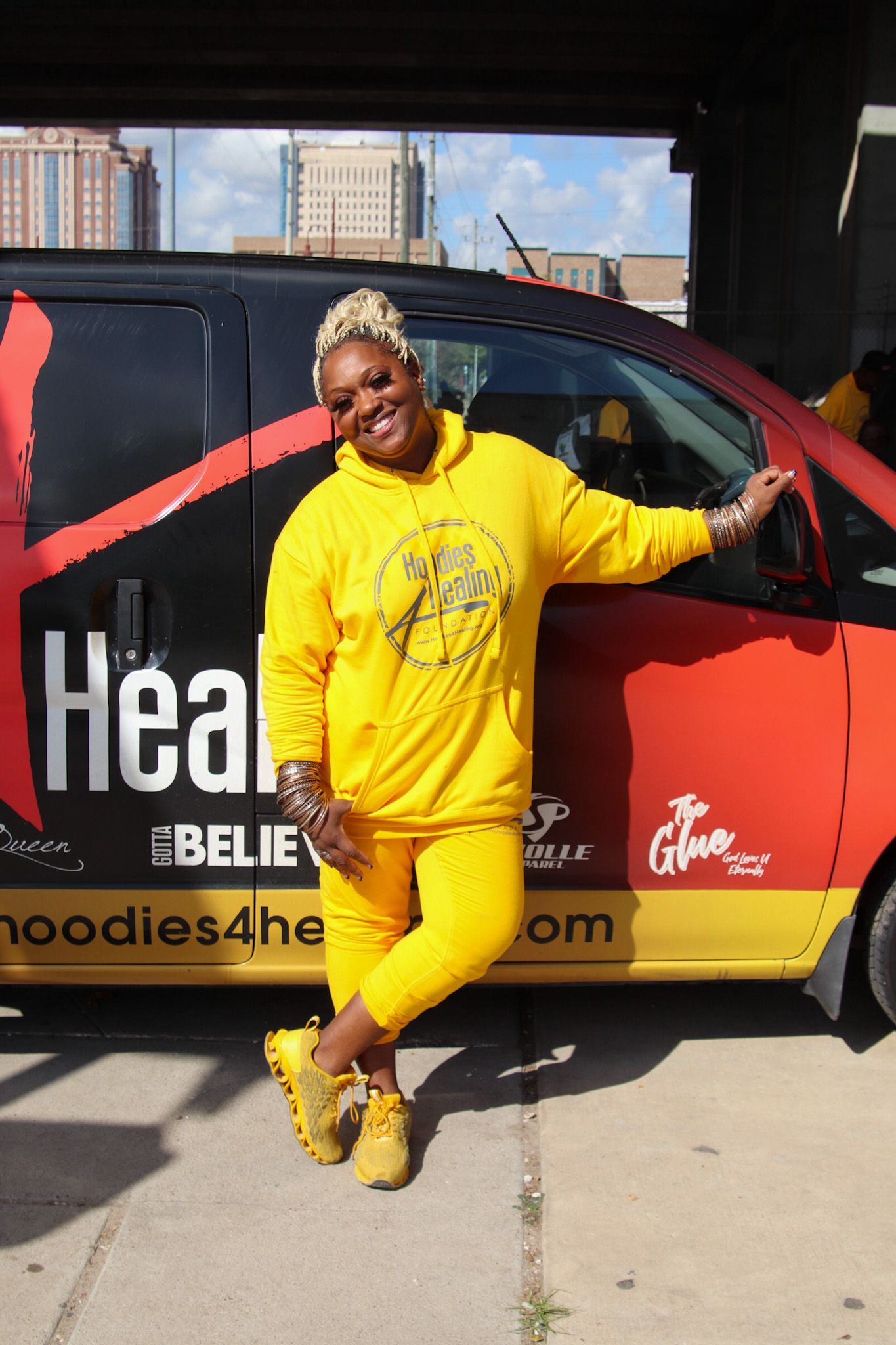 A woman in a yellow hoodie is standing in front of a red and yellow van.