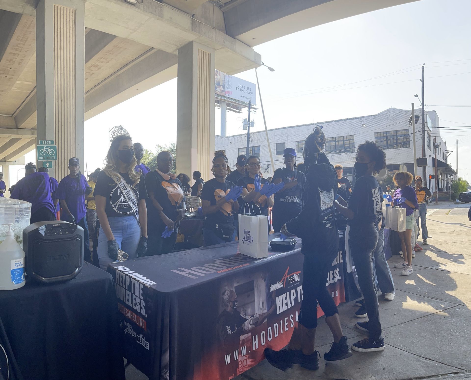 A group of people are standing around a table under a bridge.