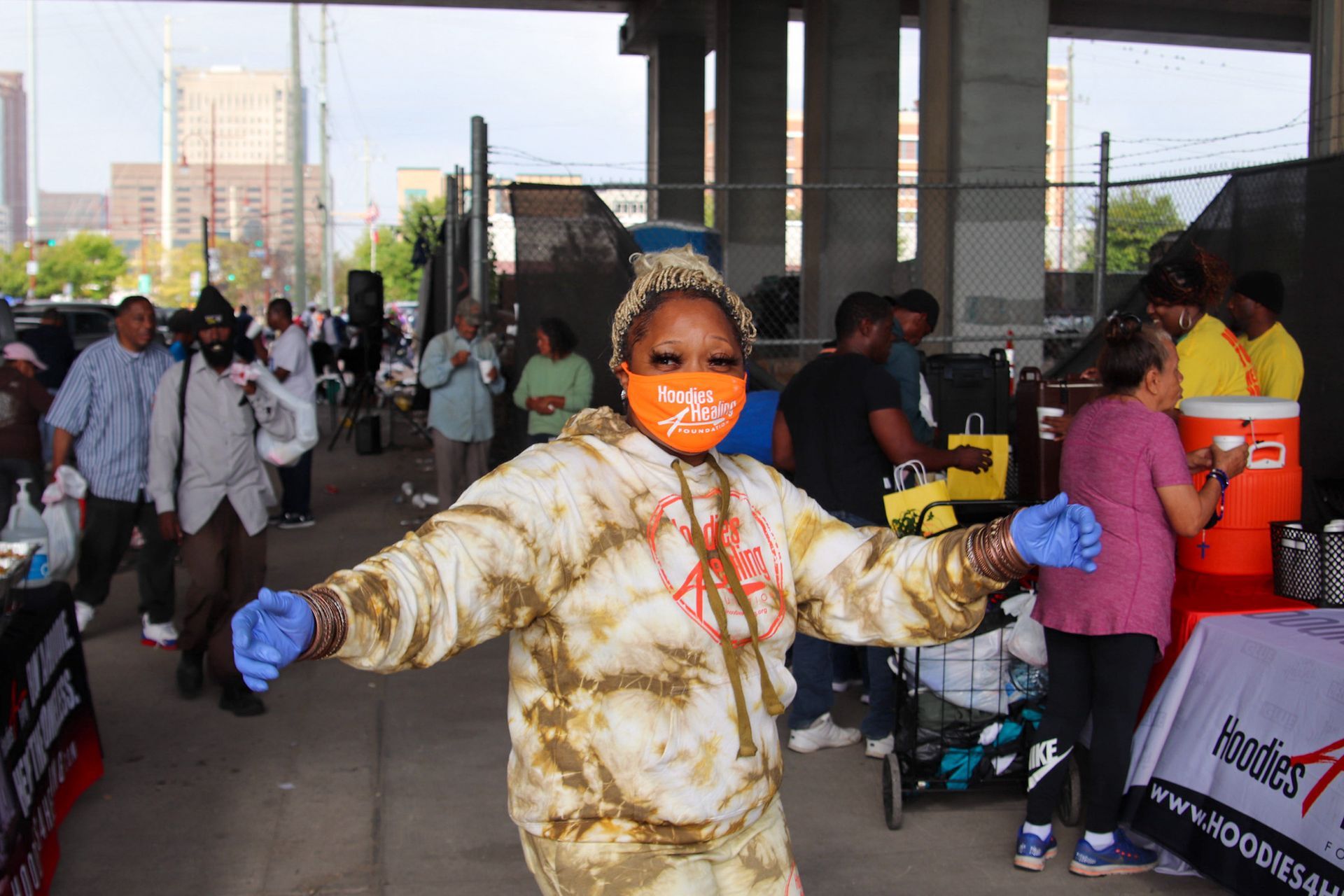 A woman wearing a mask and gloves is standing in front of a crowd of people.